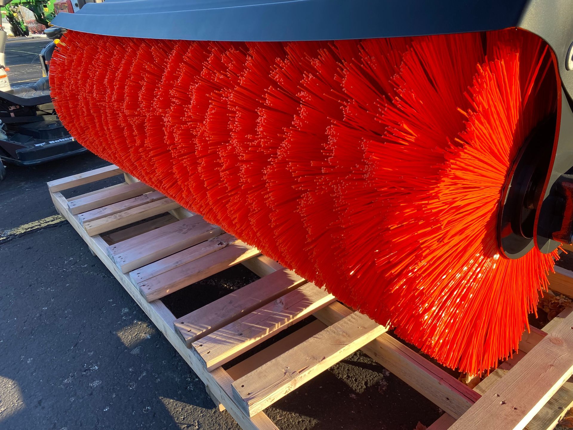 Red industrial brush on a wooden pallet, likely for road sweeping or similar maintenance.