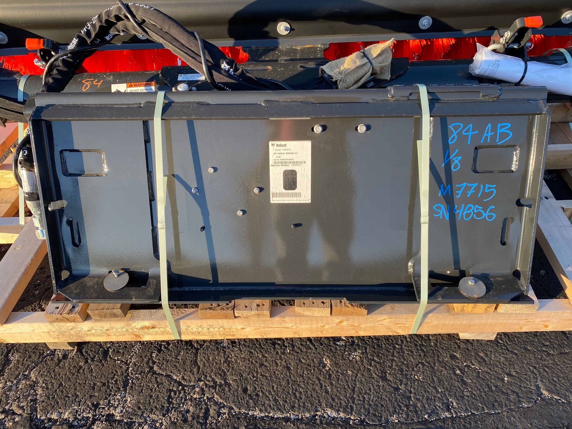 Black metal box on a wooden pallet, held with straps. Marked with blue writing.