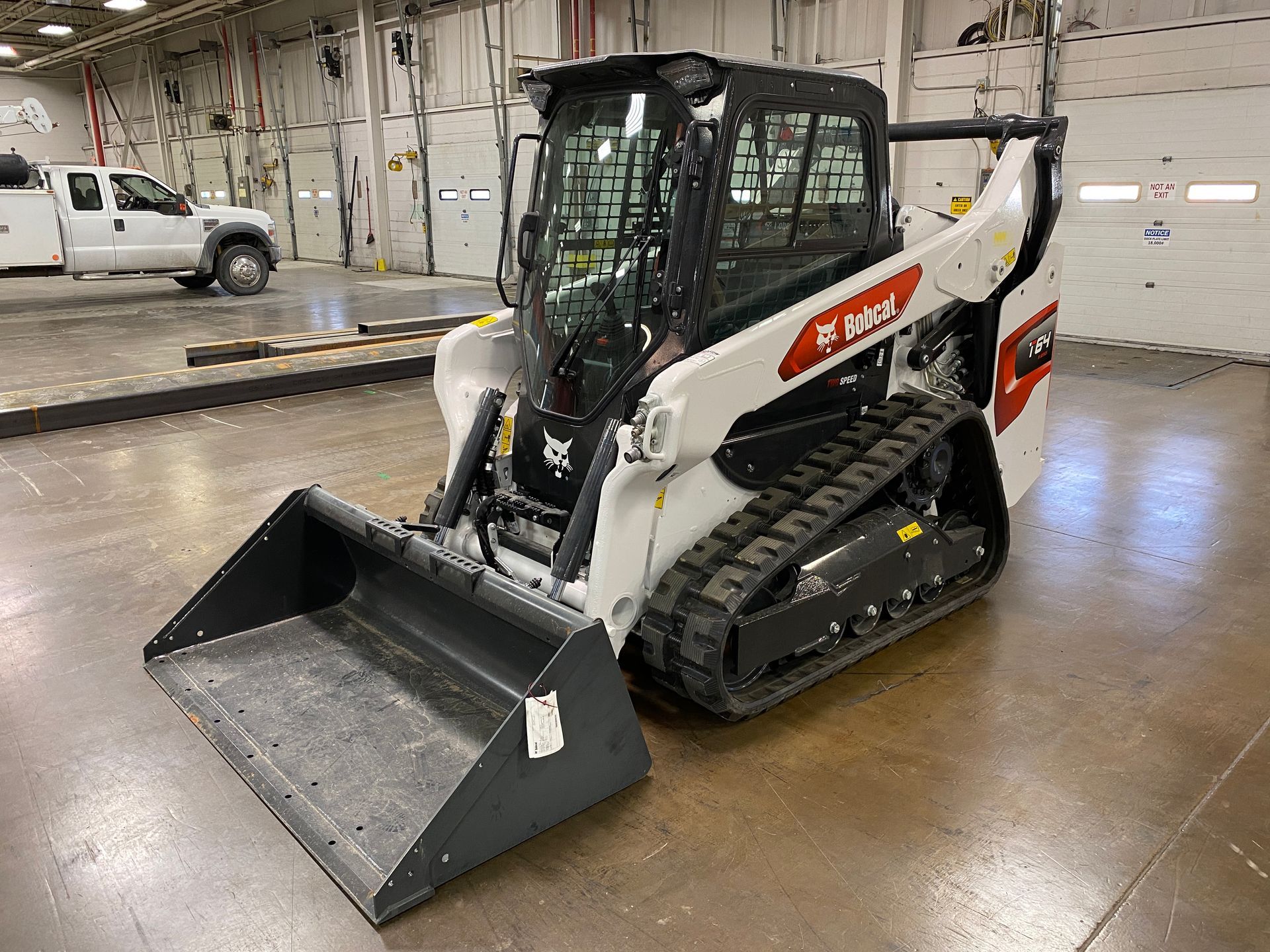 White and black Bobcat track loader in a garage setting with a front bucket.