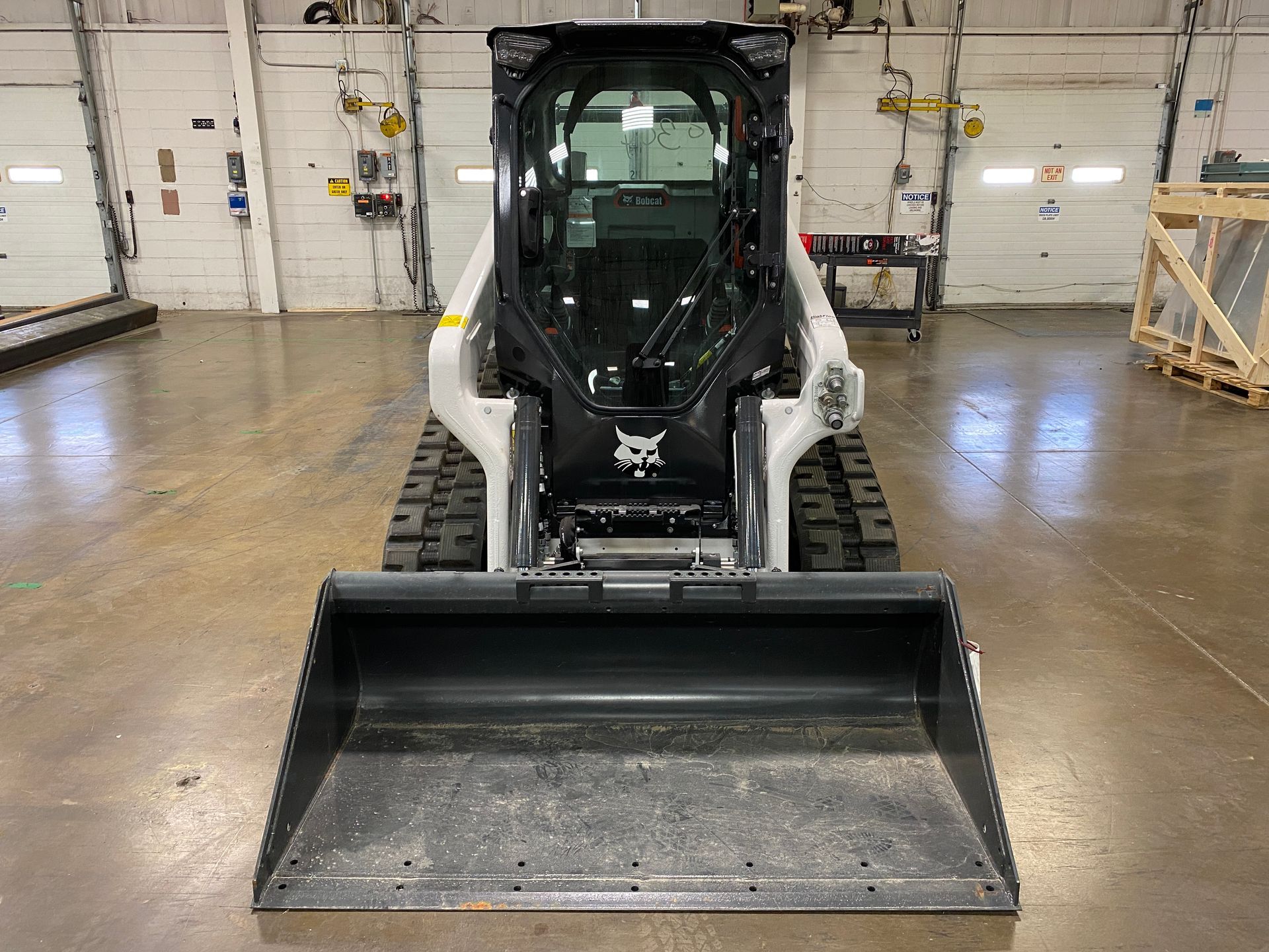 Bobcat skid-steer loader with black cab and bucket, indoors.