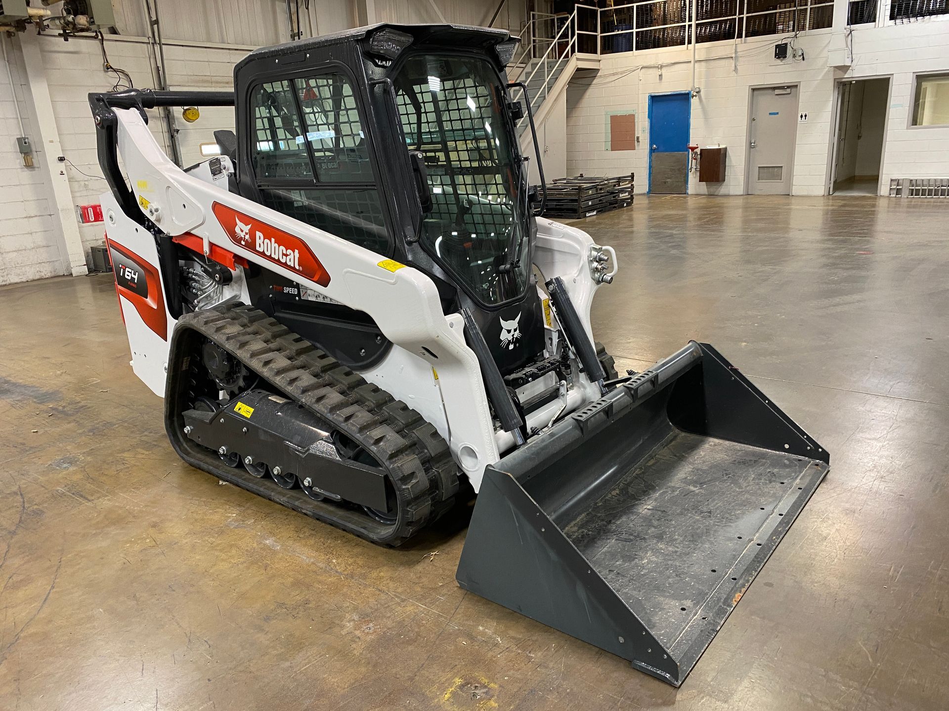 White Bobcat compact track loader with bucket in a warehouse.