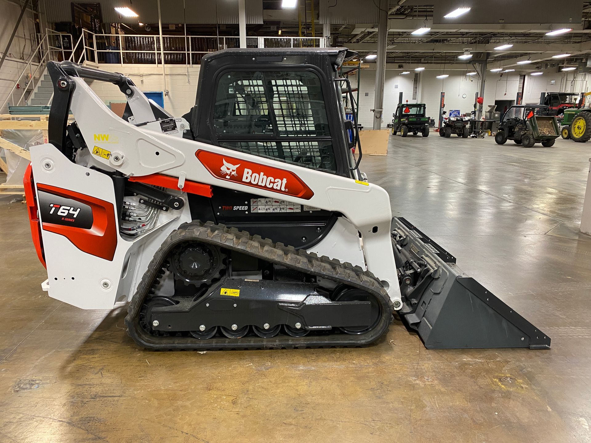 White and red Bobcat track loader with bucket in a warehouse setting.