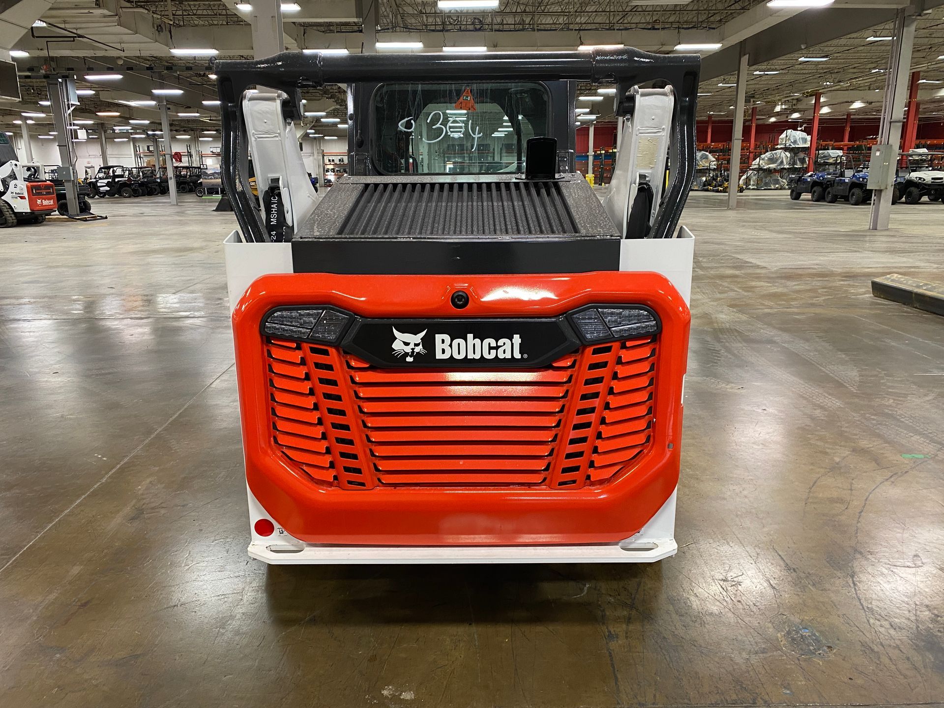 Orange and black Bobcat skid-steer loader, front view, in a warehouse setting.