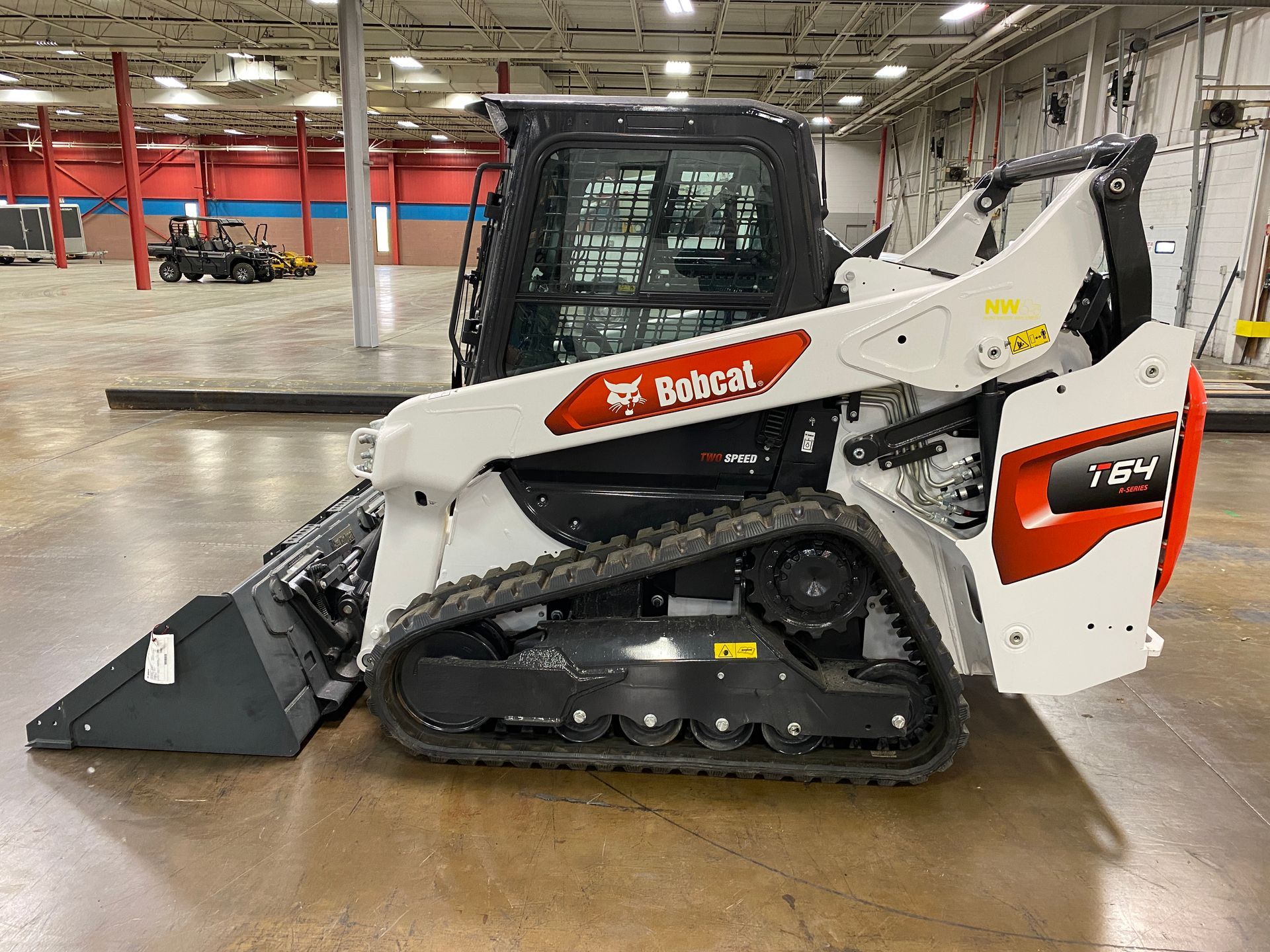White Bobcat T64 compact track loader with bucket in a warehouse.