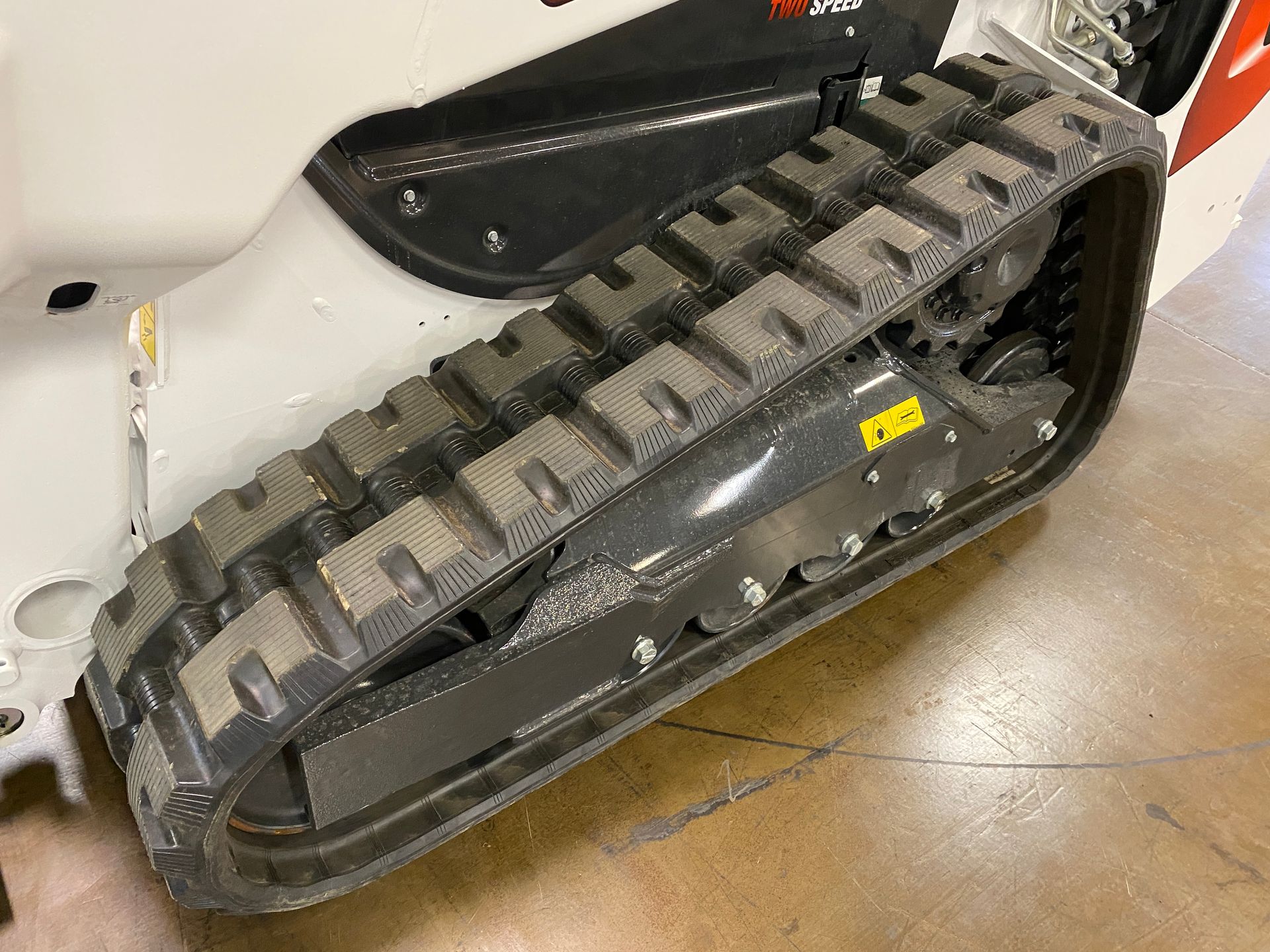 Close-up of a black rubber track on a white skid steer loader. The track has a repeating tread pattern.