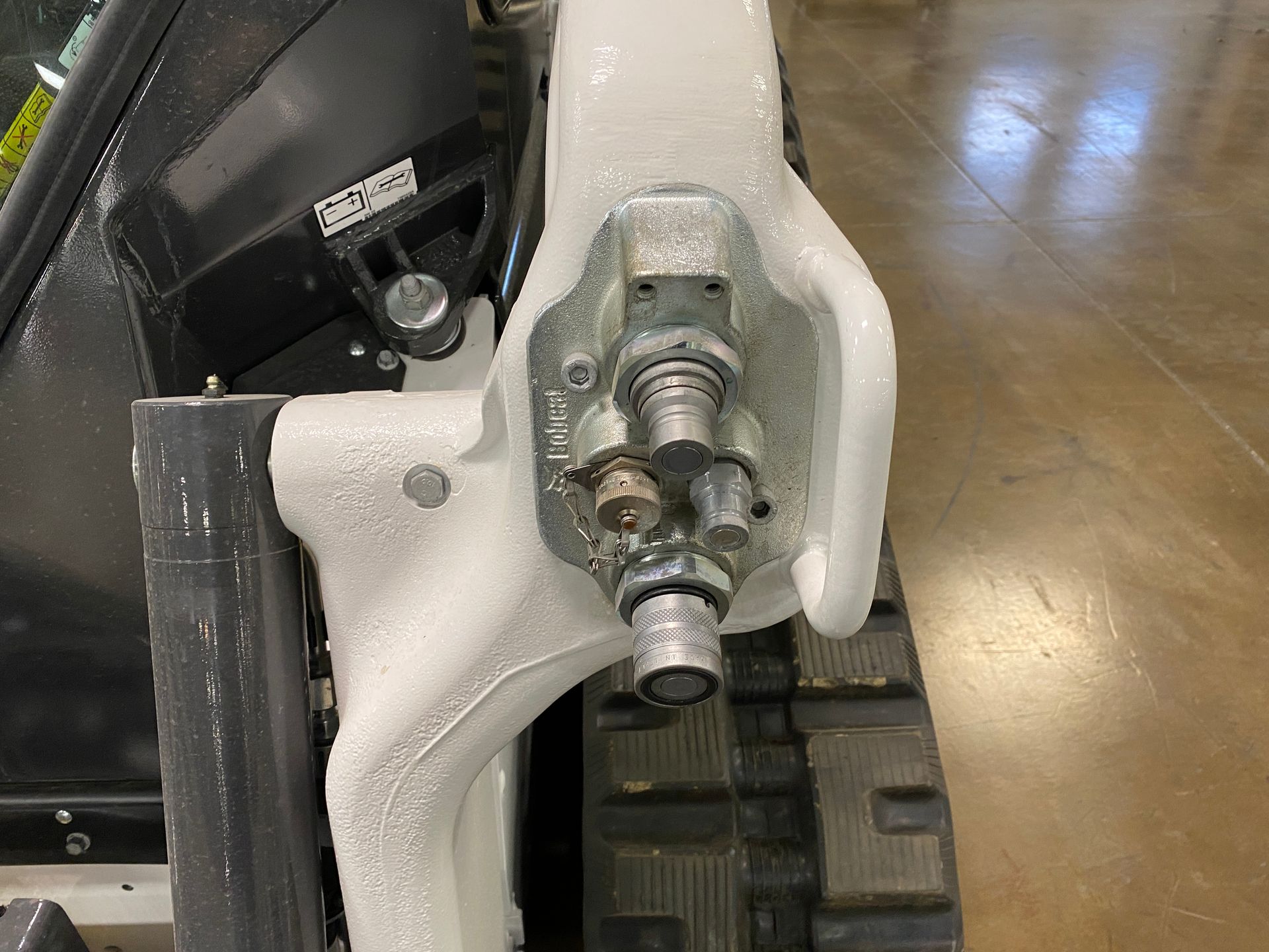 Close-up of a white skid steer arm with hydraulic fittings; a black track is visible below.