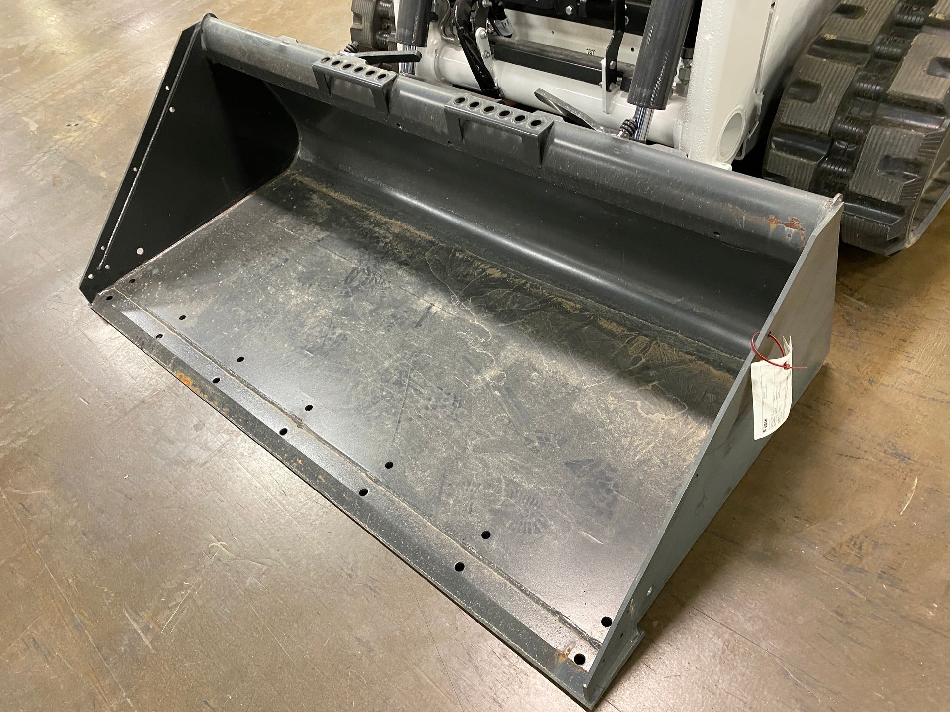 Gray skid steer bucket on a concrete surface.