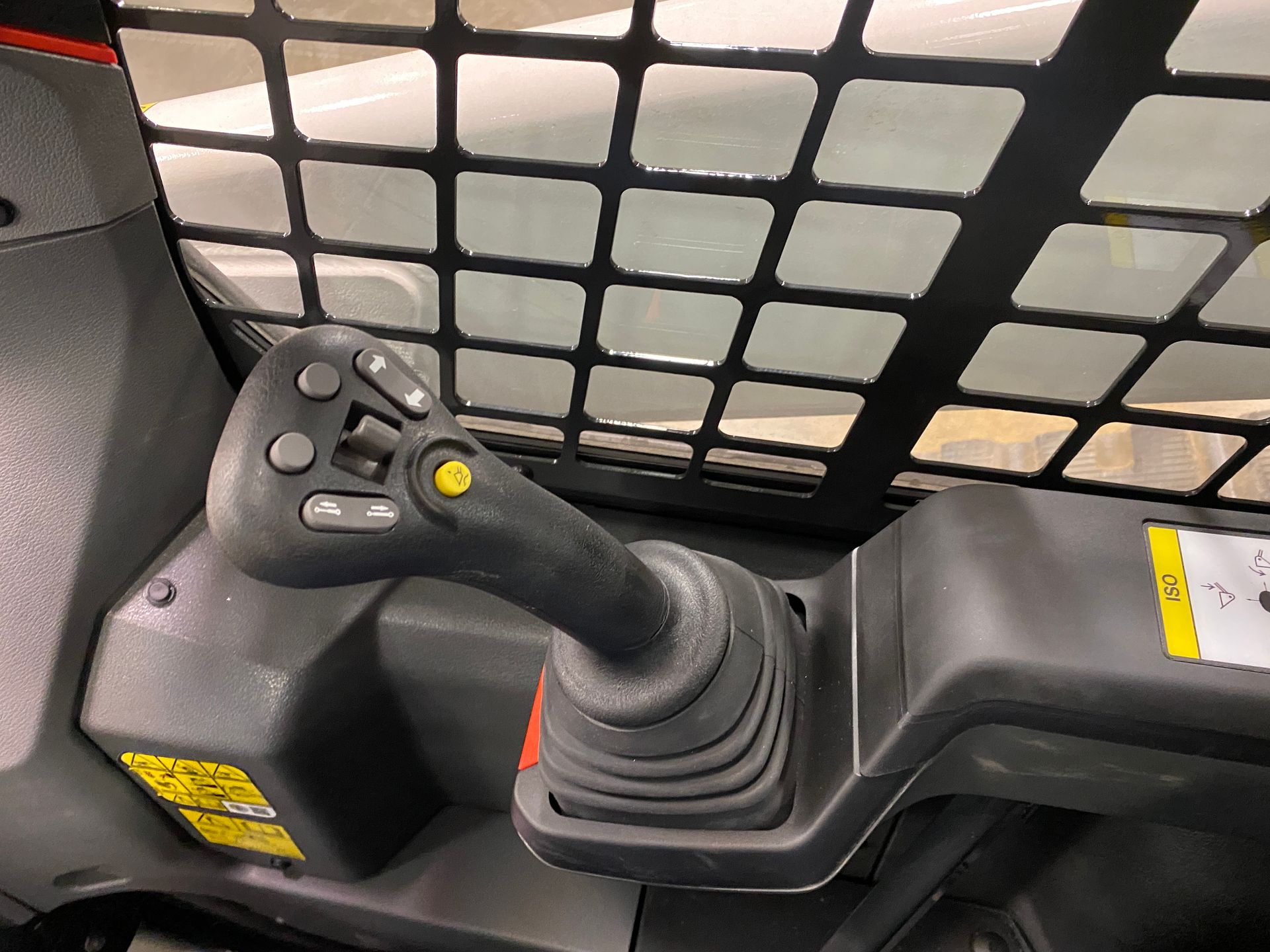 Joystick control inside a vehicle cab with a black safety grate in the background.