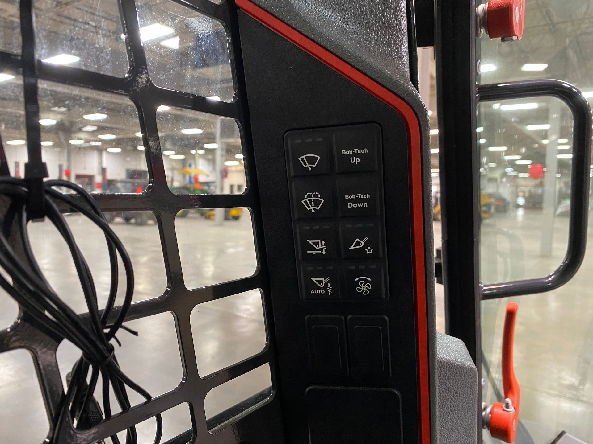 Control panel with illuminated switches in a skid steer cab. Black panel with red accents.