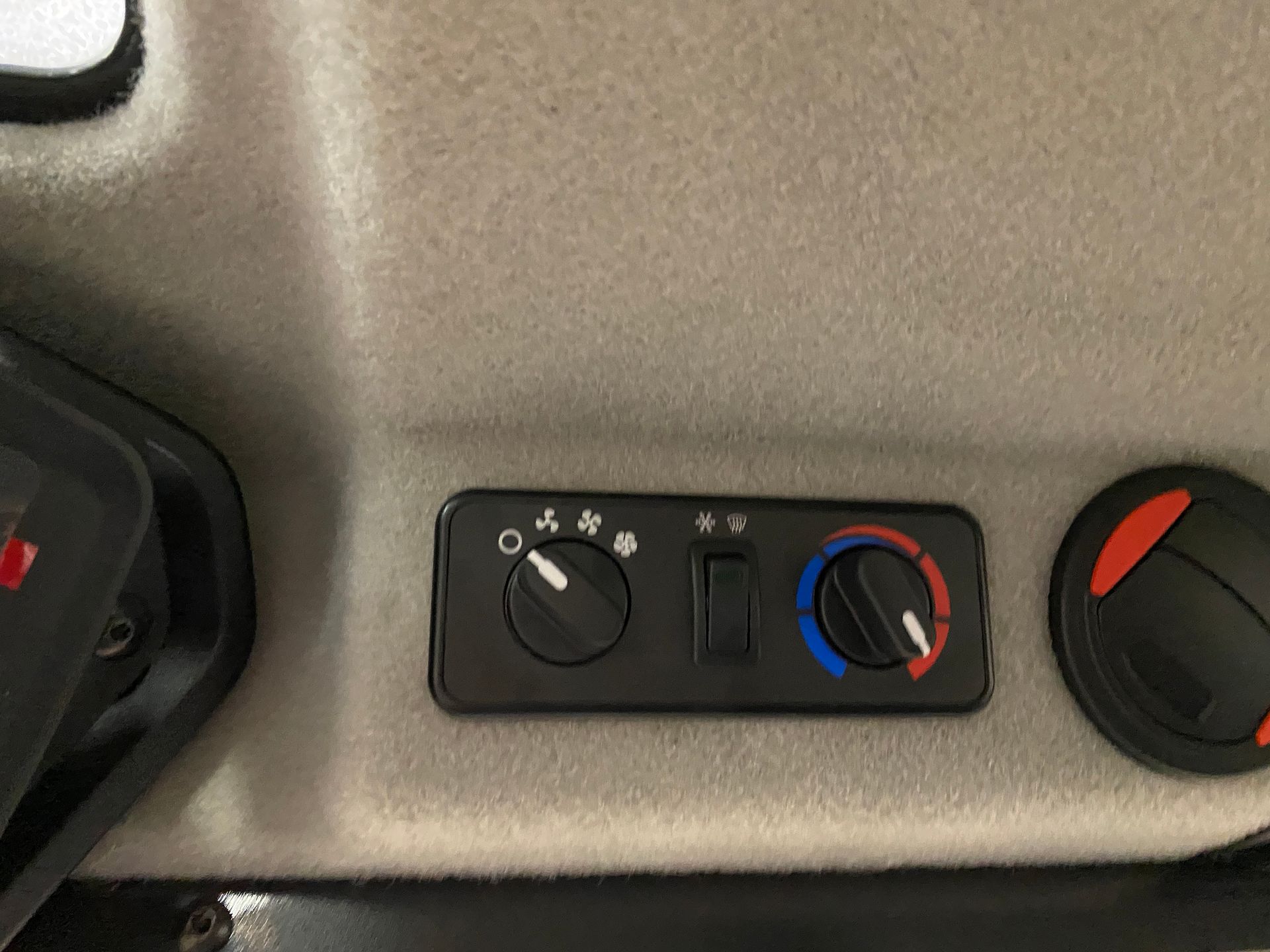 Black control panel with HVAC controls in a vehicle, against a light gray interior.
