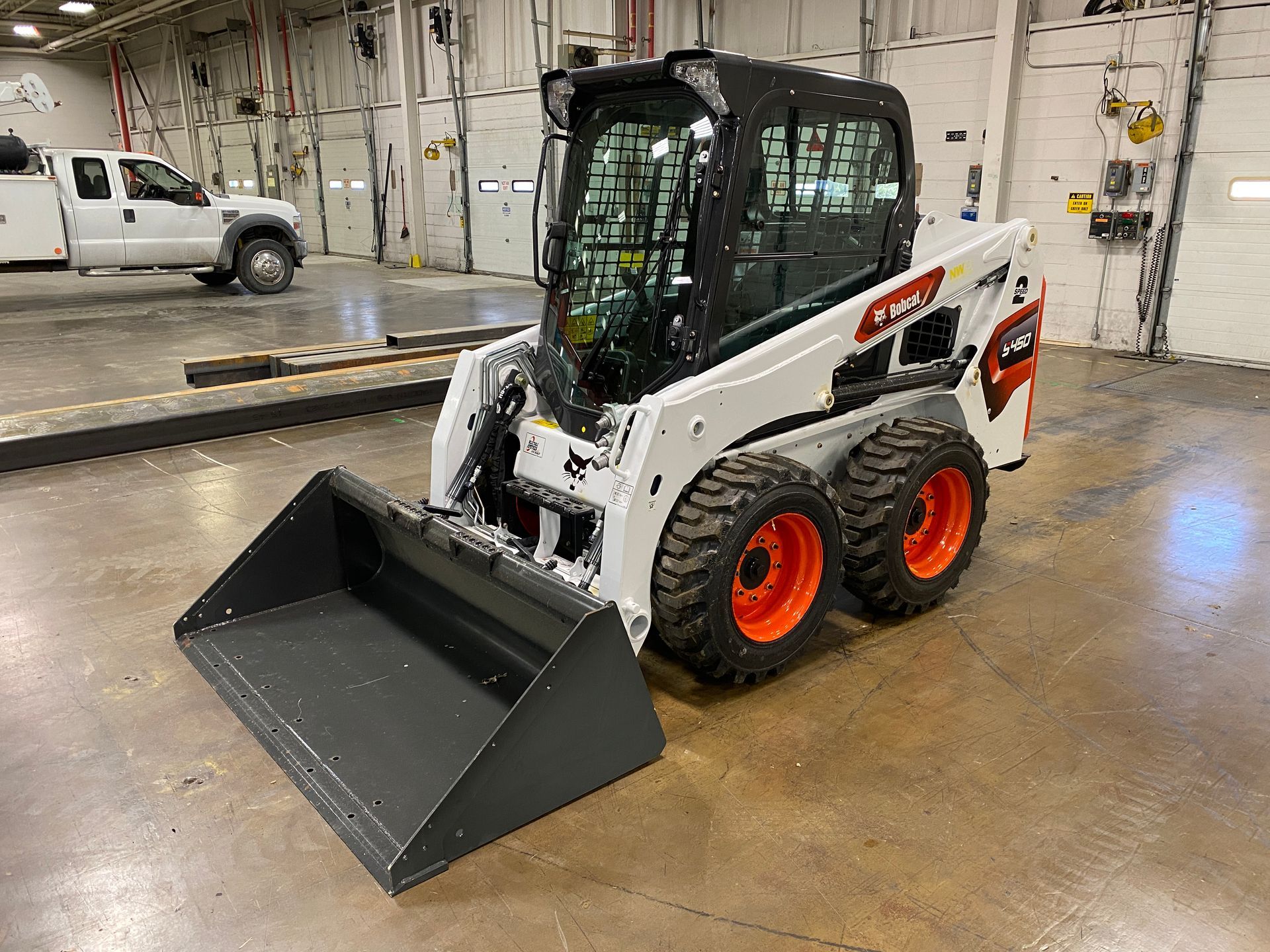 White and black Bobcat skid-steer loader with a bucket in a garage.