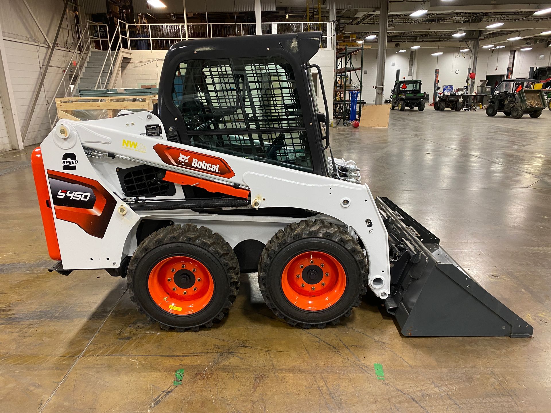 Bobcat S450 skid-steer loader, white and orange, on a factory floor.