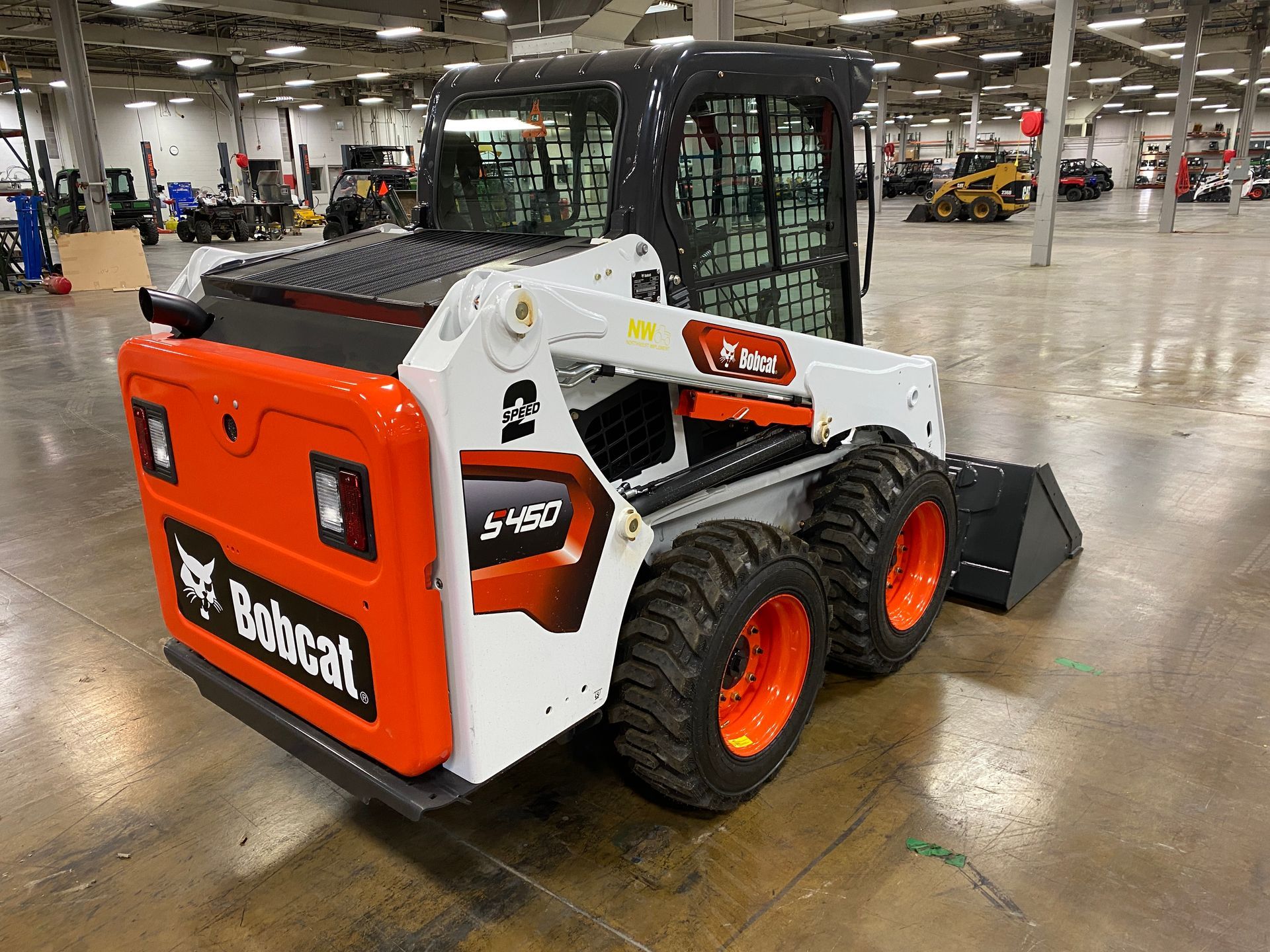 A Bobcat S450 skid-steer loader, white and orange, inside a warehouse.