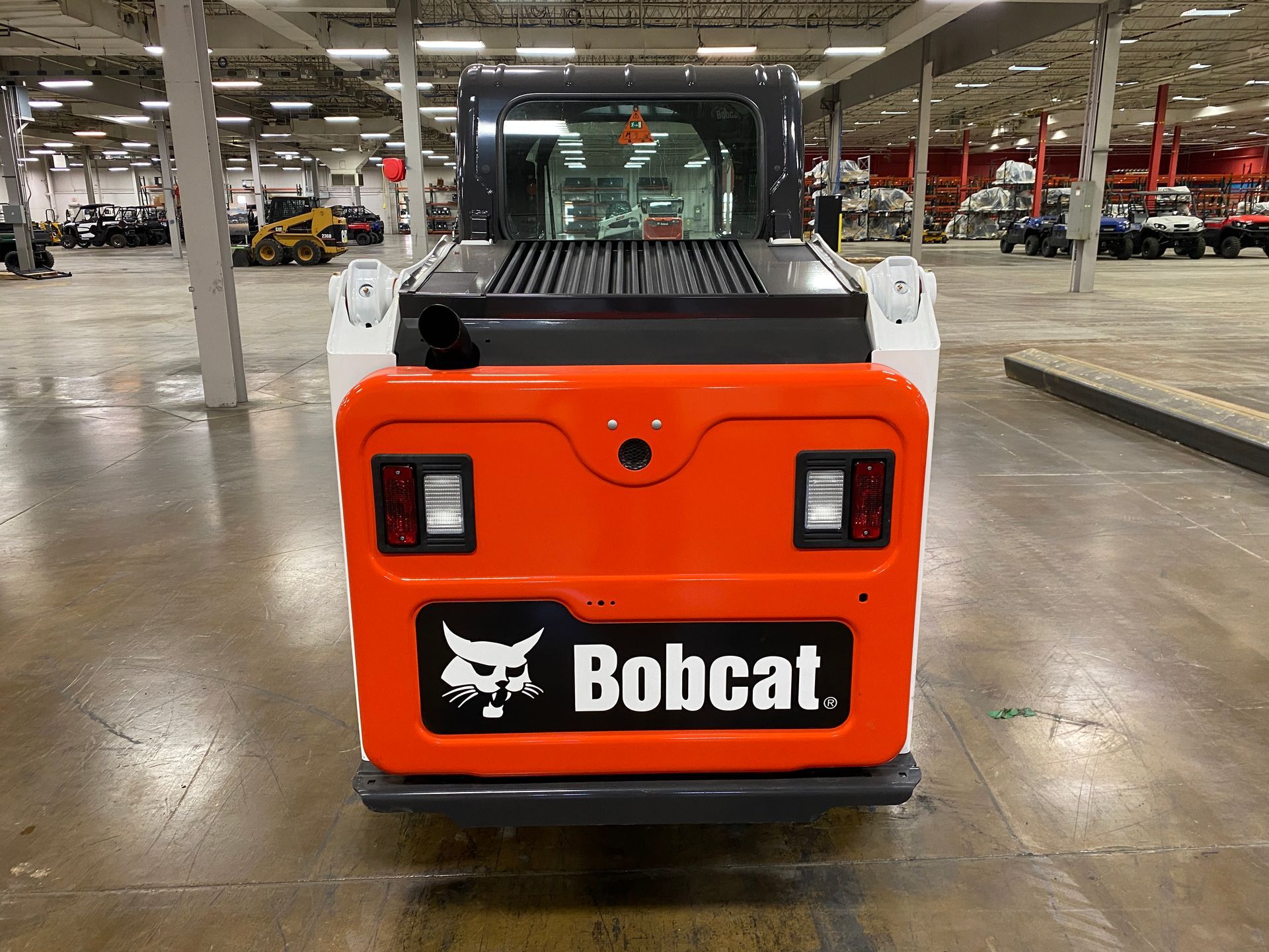 Rear view of an orange and white Bobcat skid steer loader, indoors.