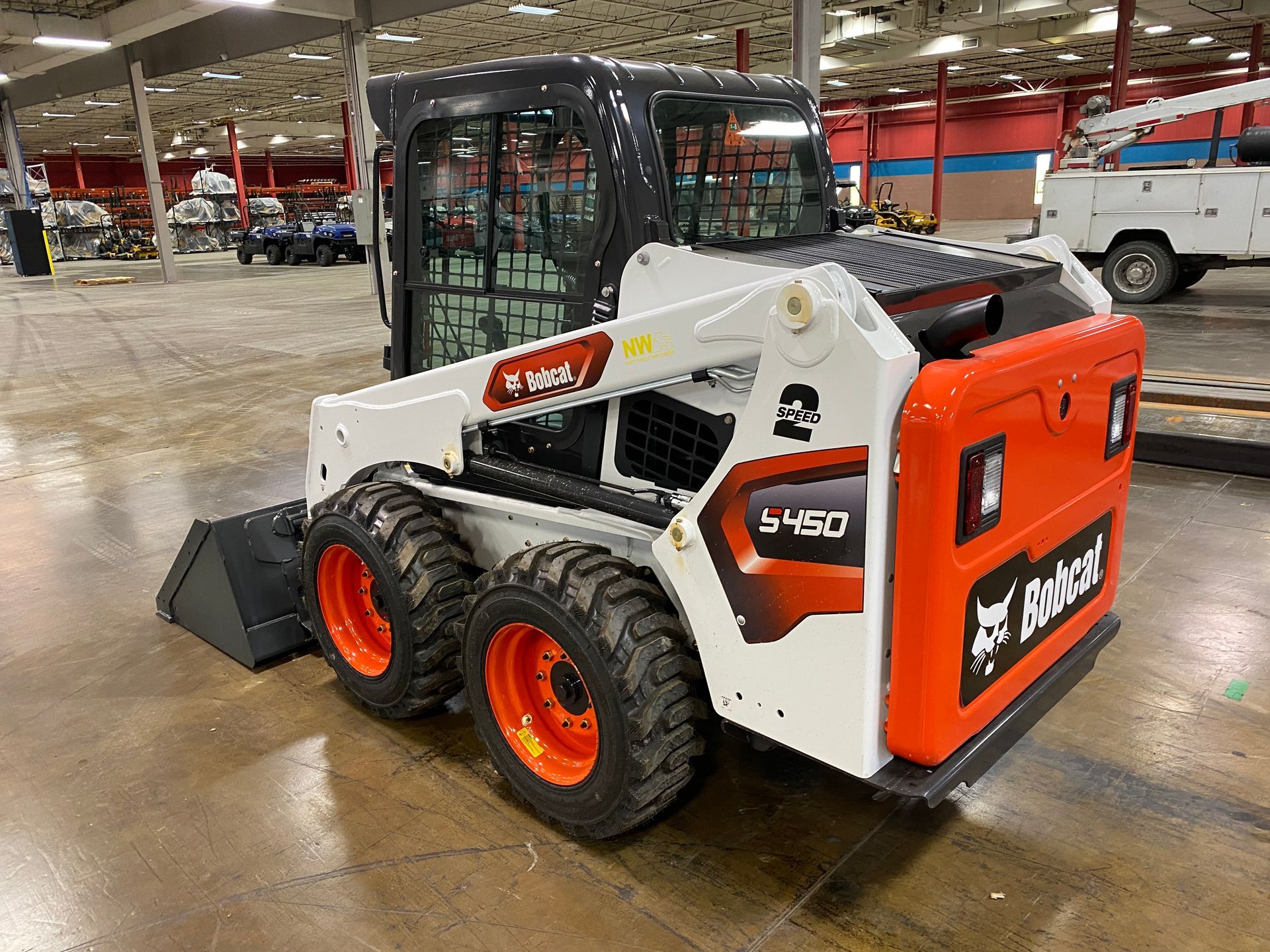 Bobcat T450 skid-steer loader, white with orange wheels, sitting in a warehouse.