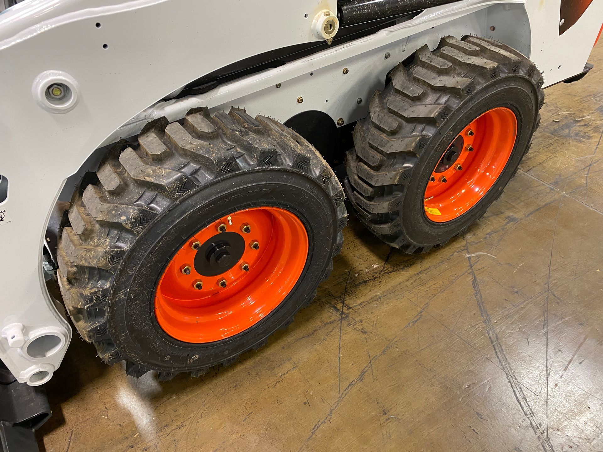 Two black tires with orange rims on a white Bobcat skid steer machine.