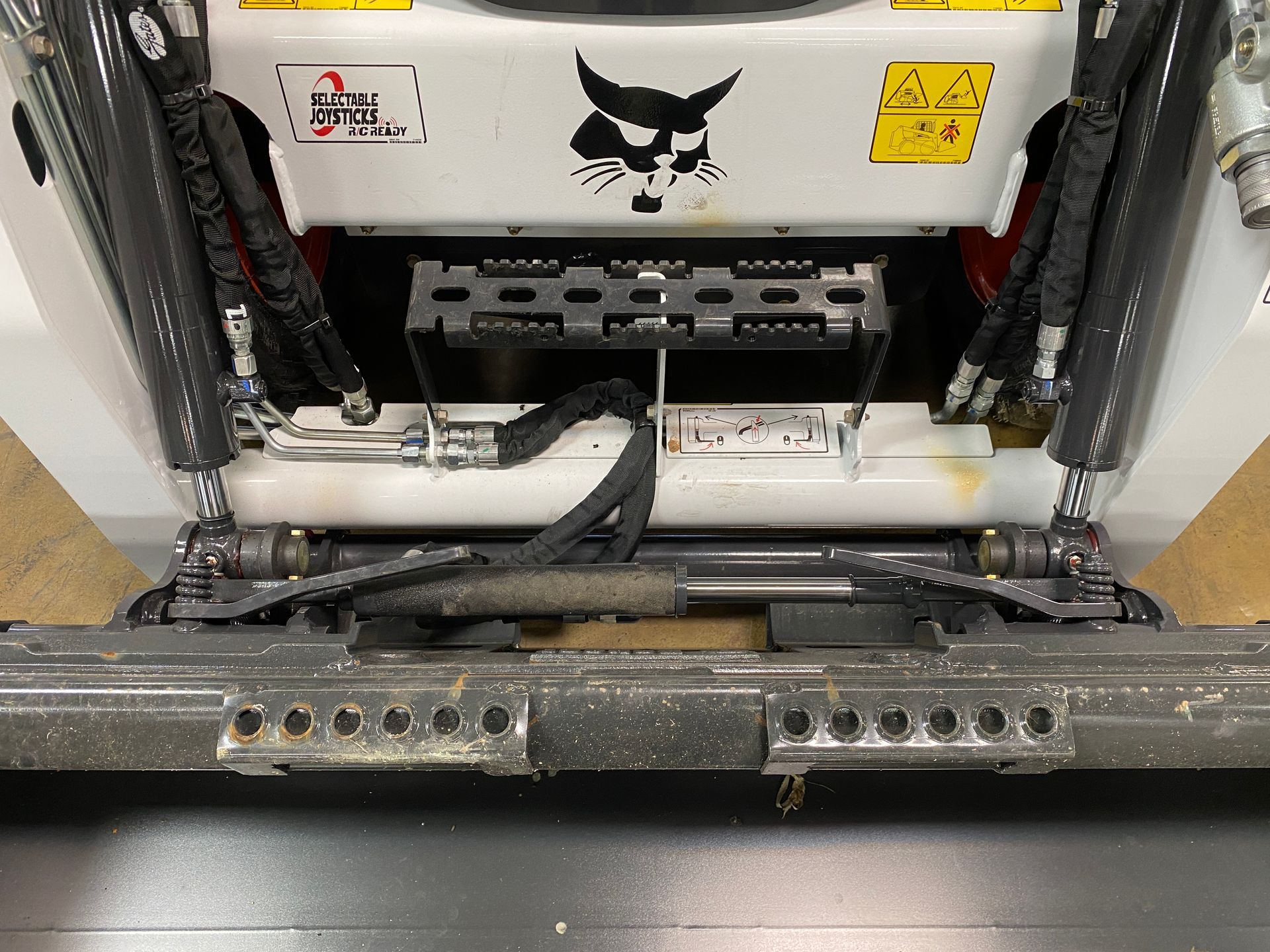 A close-up of a Bobcat skid-steer loader's lift arm and attachment mechanism, with the Bobcat logo visible.