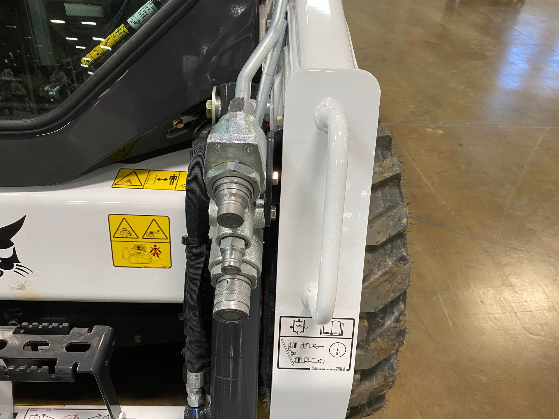 A white Bobcat skid-steer loader, showing hydraulic lines, a handhold, and a tire.