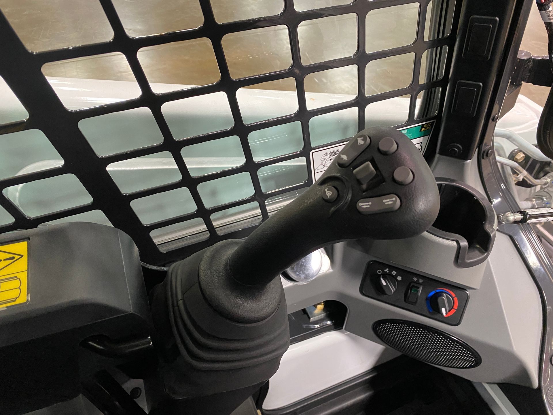 Interior view of a skid steer operator's control panel. A joystick with buttons sits in the foreground.