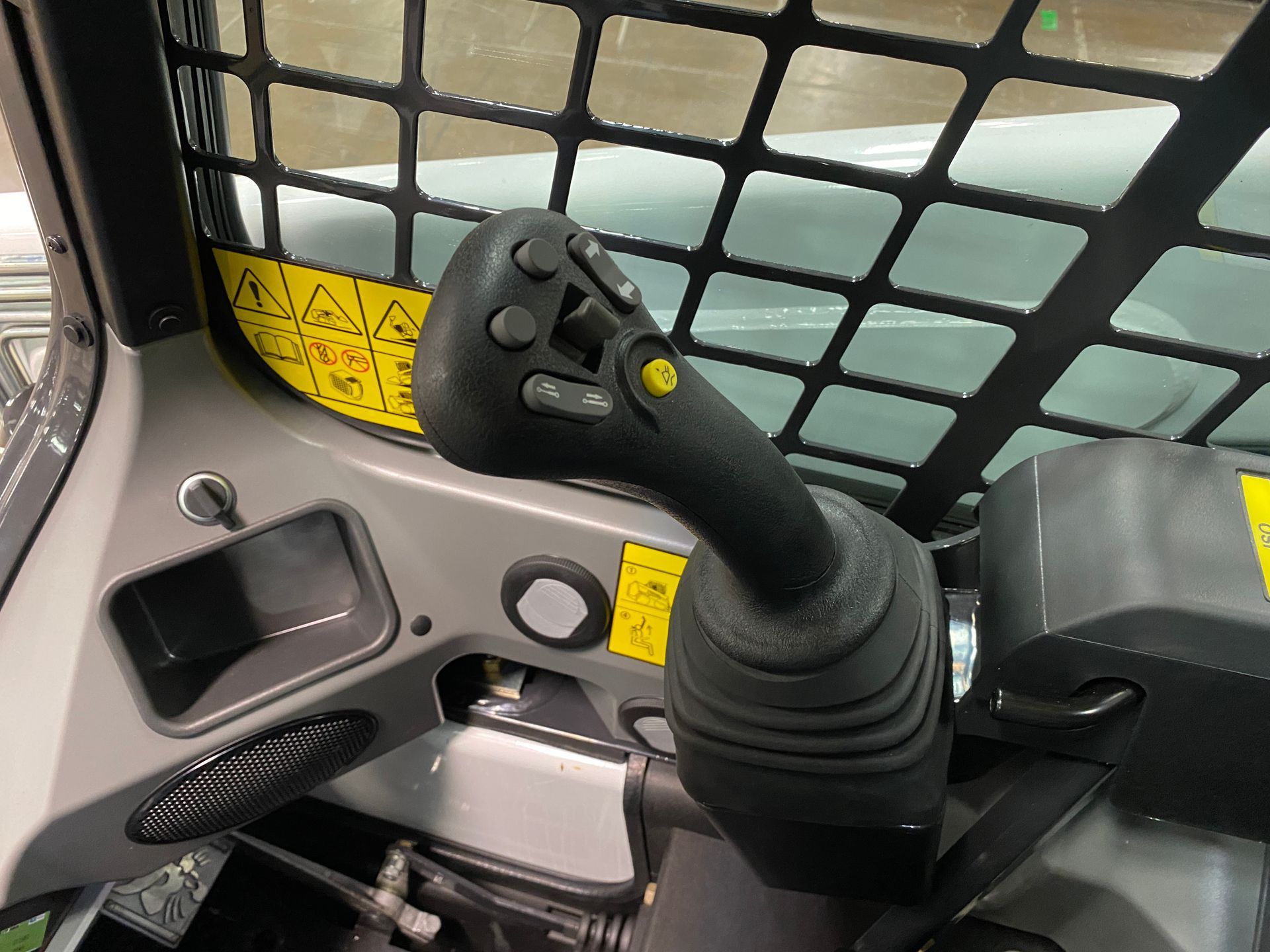 Close-up of a skid steer joystick with buttons and controls, inside the cab with a protective screen.