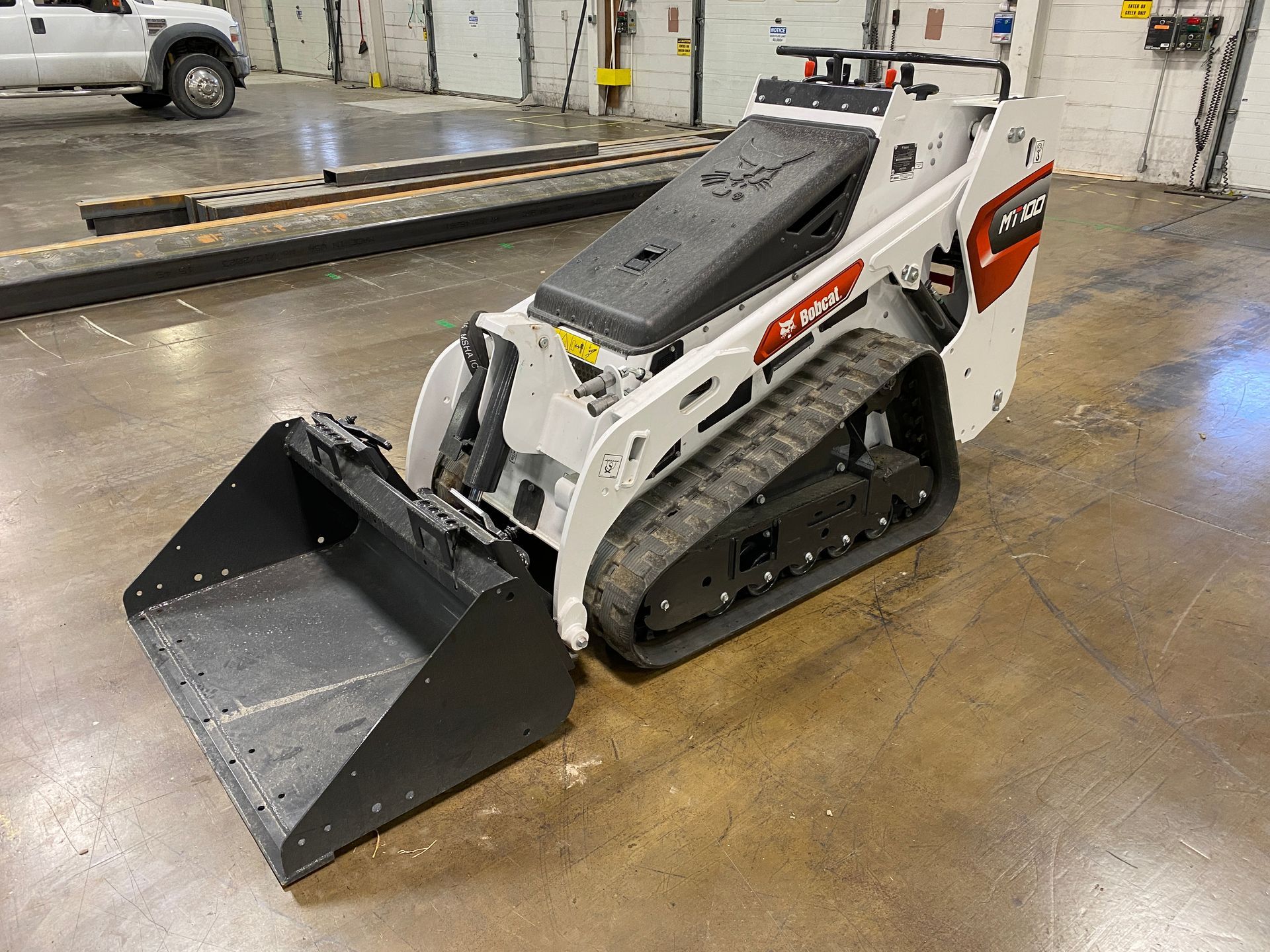 White and red Bobcat track loader with bucket in a warehouse setting.