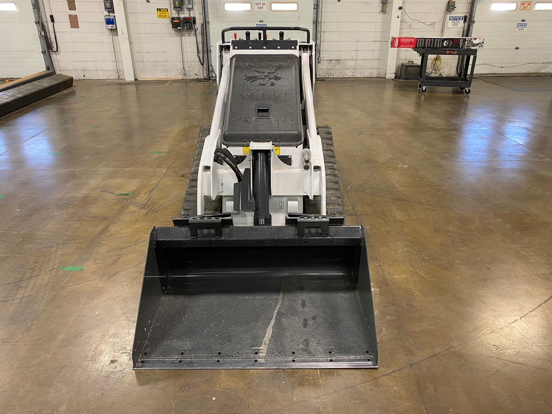 White and black skid steer loader with bucket in a garage.