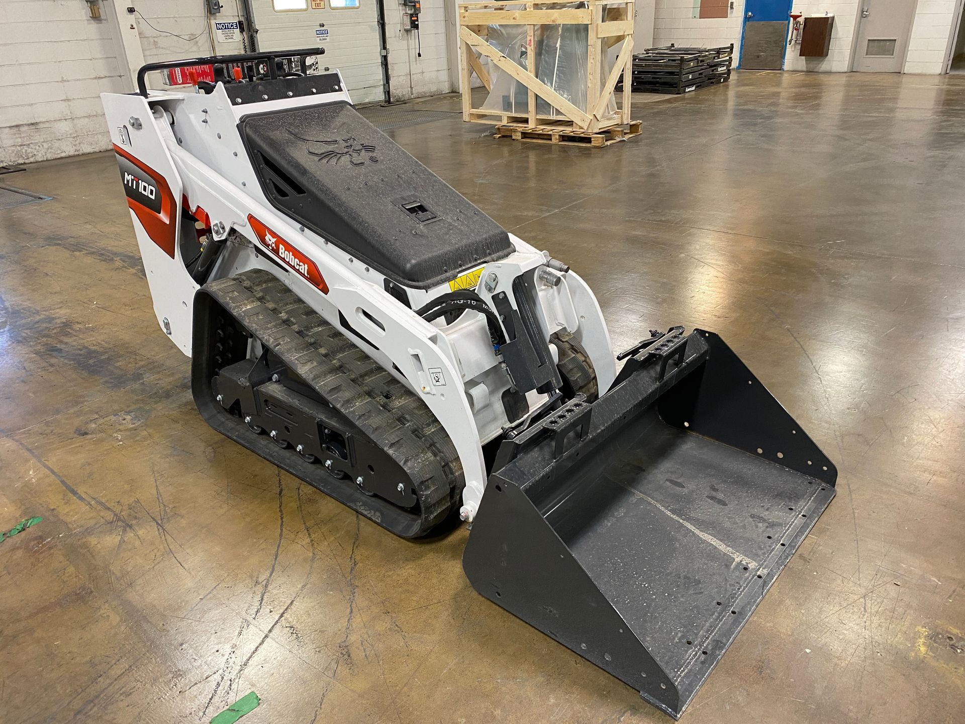 White Bobcat compact track loader with bucket in a warehouse.