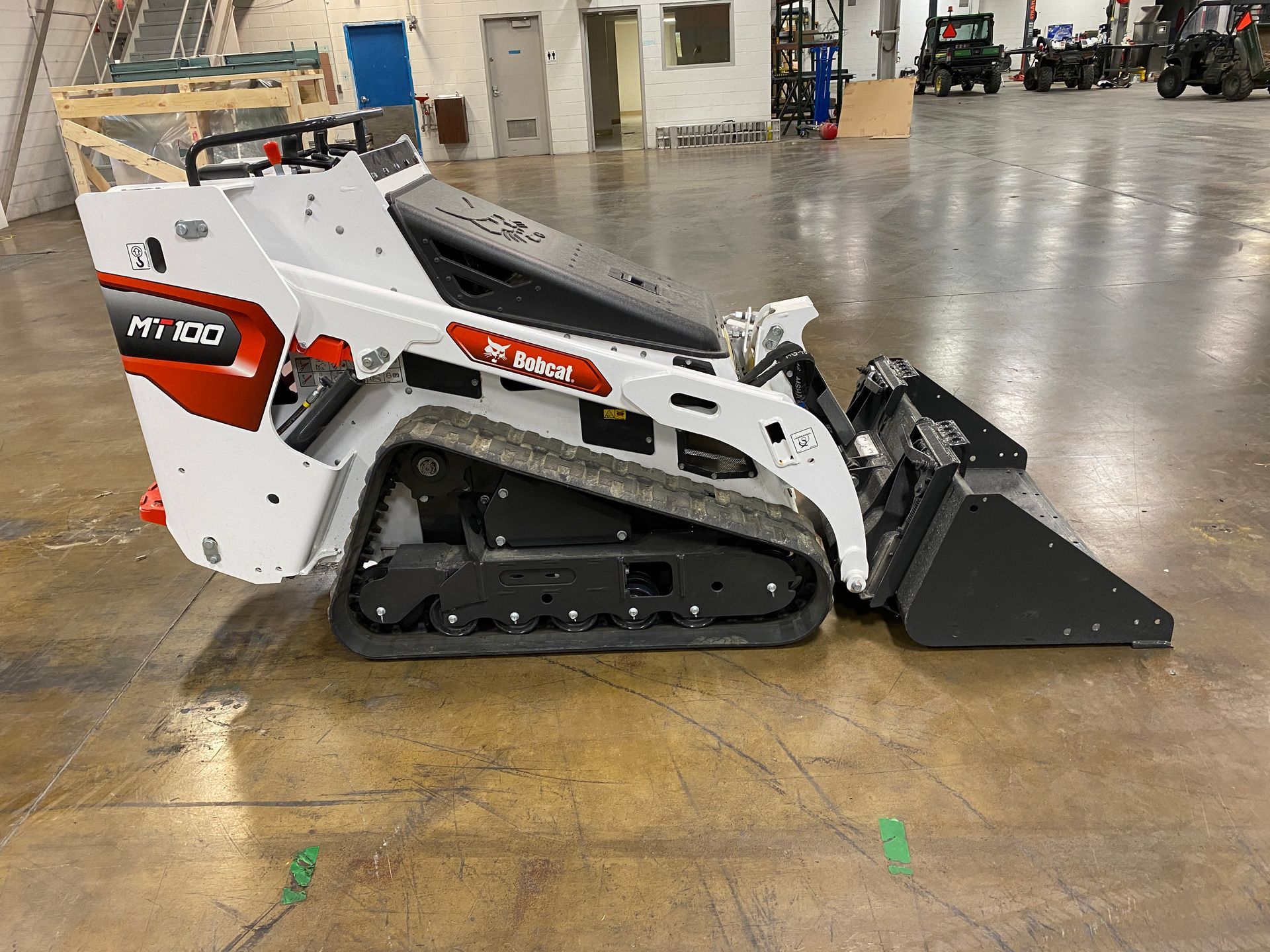 Bobcat MT100 compact track loader with bucket in a warehouse. White, red, black.