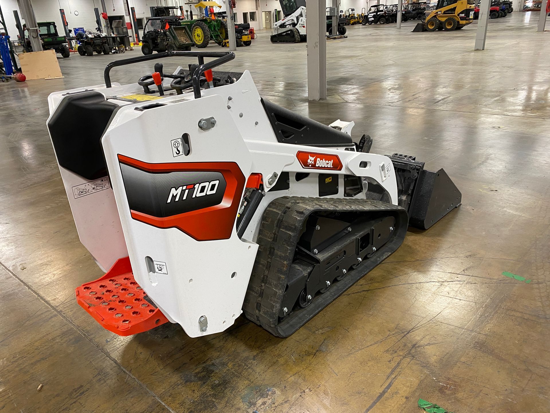 White and red Bobcat MT100 mini track loader on a concrete floor.