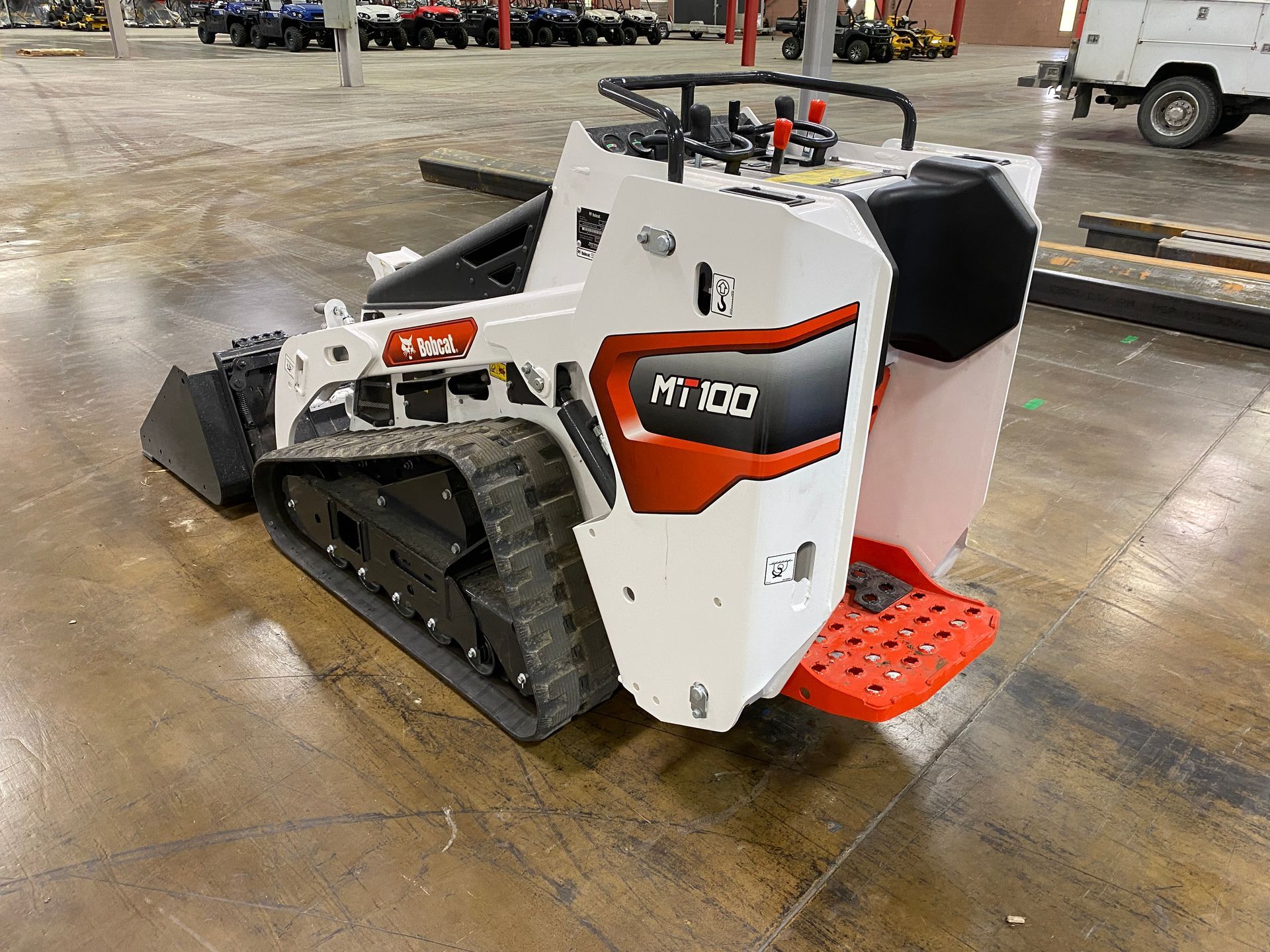 White and orange Bobcat skid-steer loader, front view. Operator compartment has black seats, red access steps.