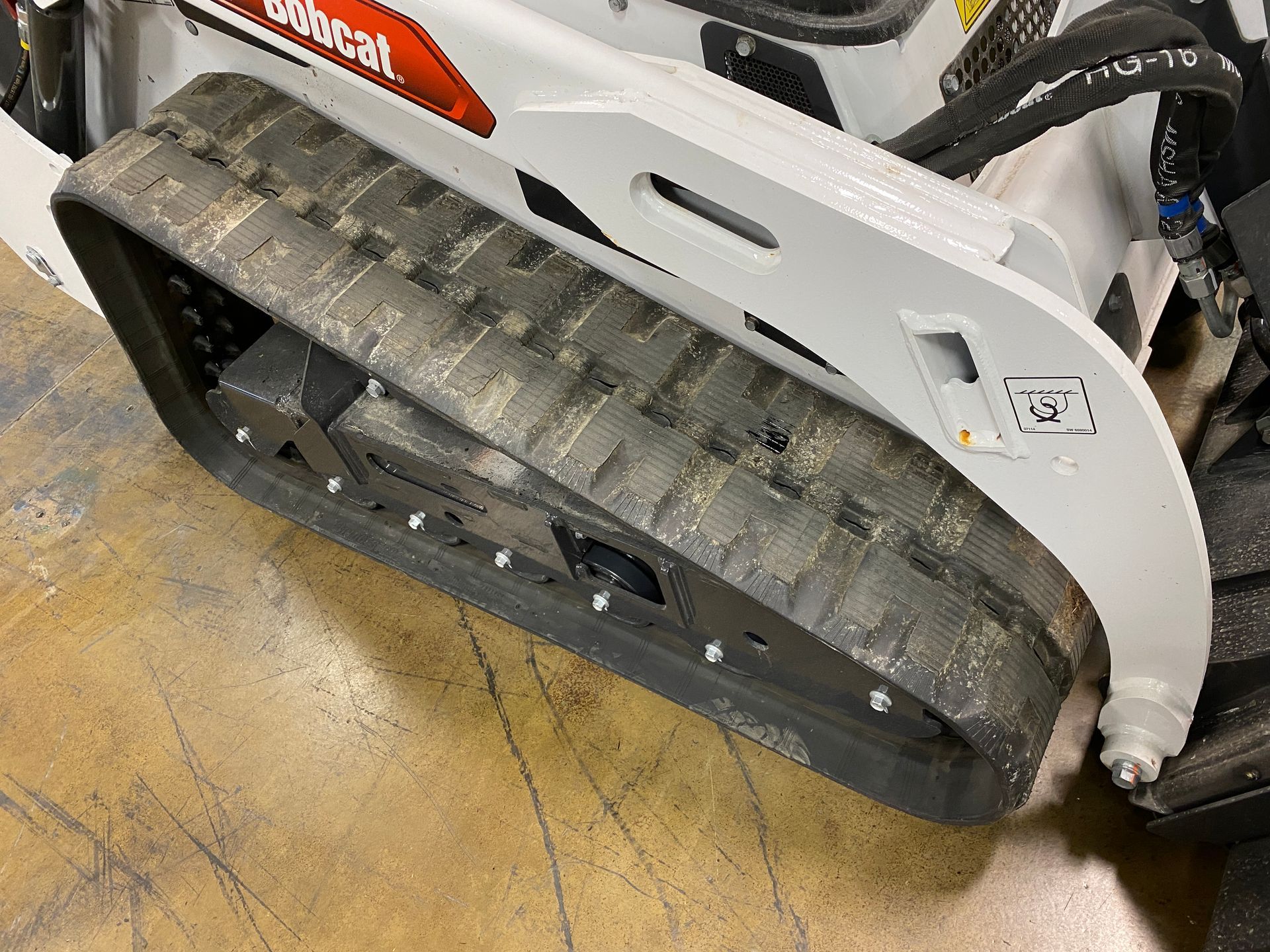Bobcat skid-steer track on concrete floor, showing rubber treads and white metal frame.