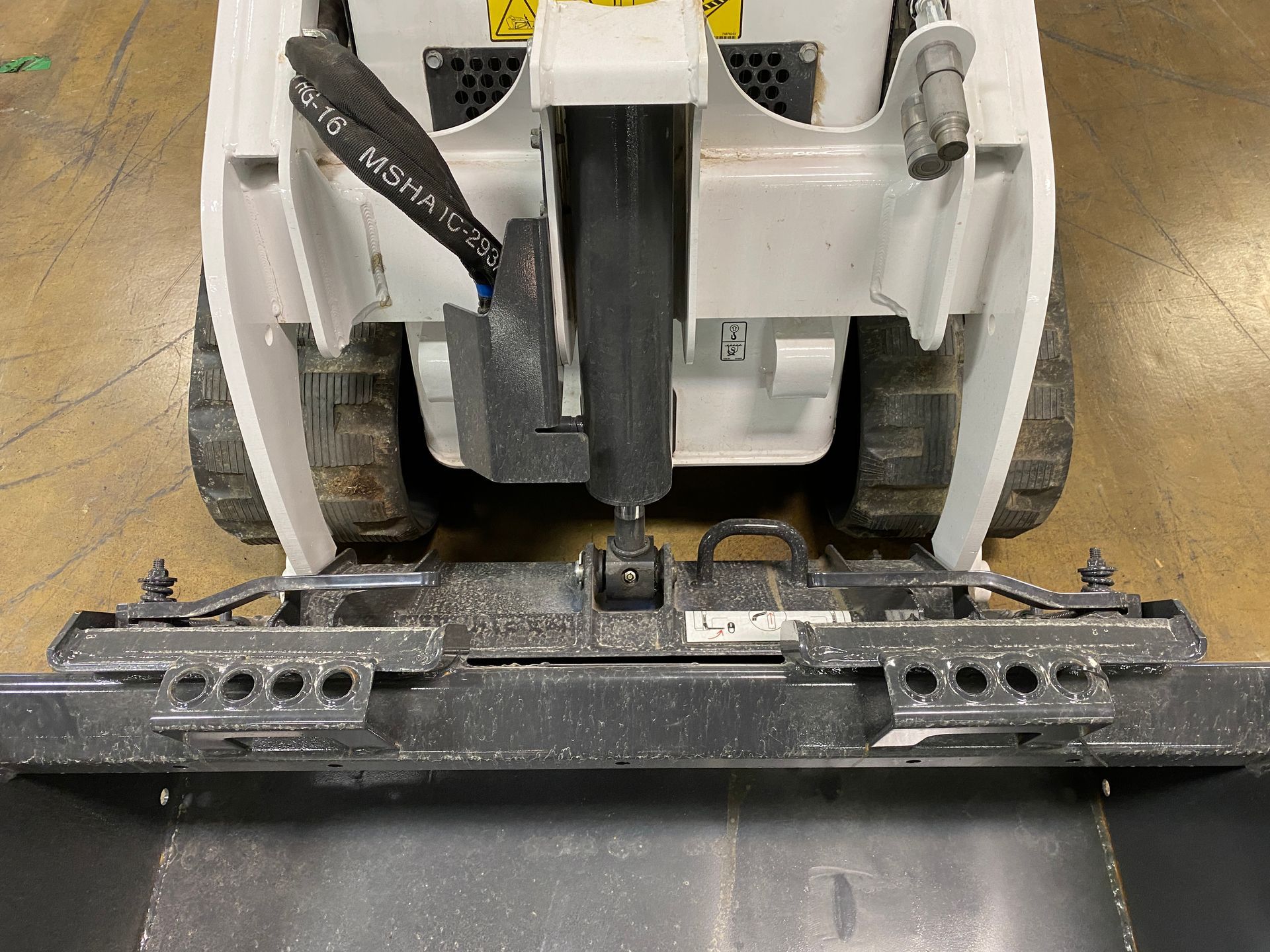 View from the front of a white Bobcat skid steer. A black attachment is connected.