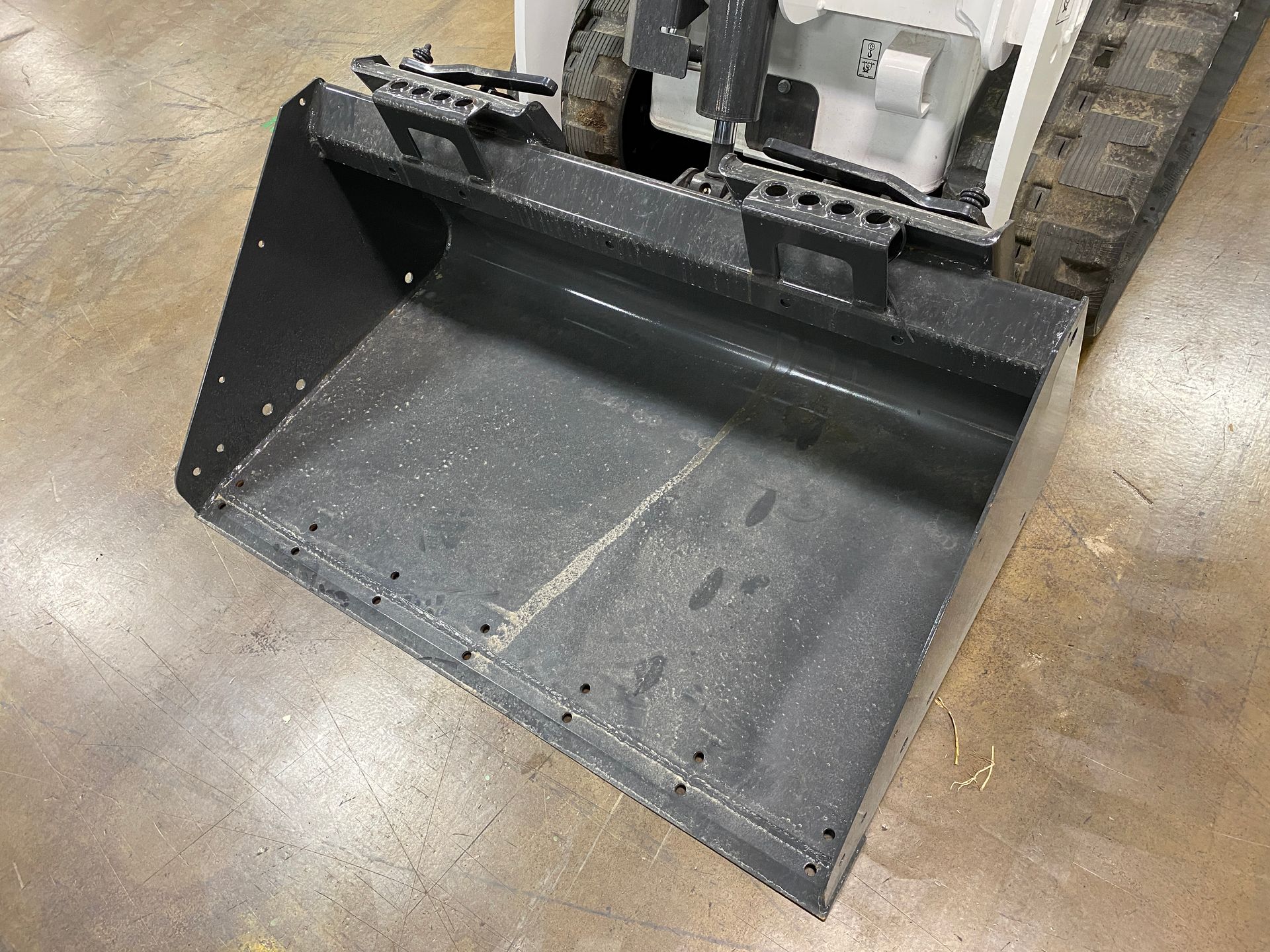 Gray bucket of a small tracked machine on a concrete floor.