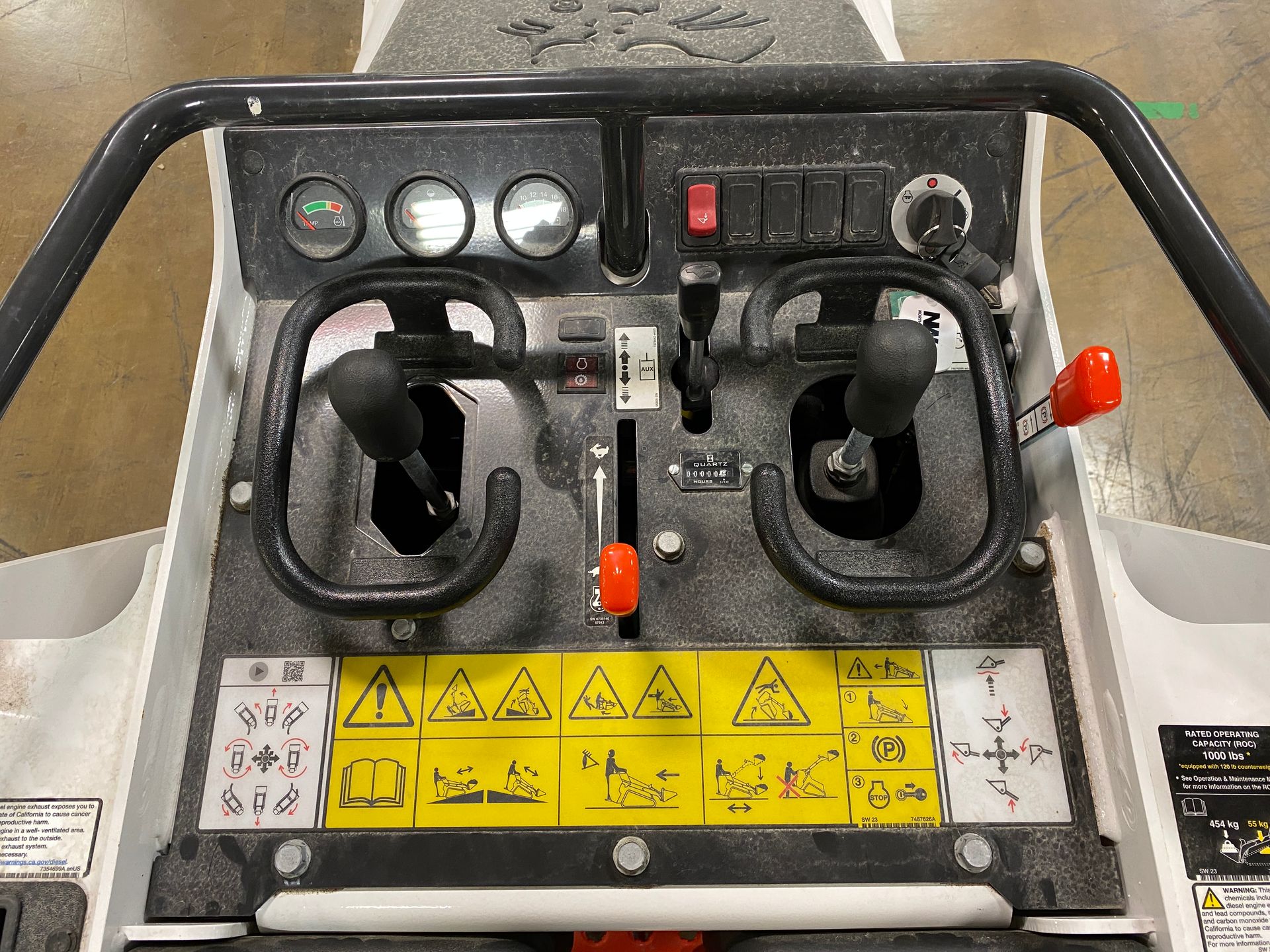 Control panel of a white skid steer, featuring joysticks, gauges, switches, and safety symbols.