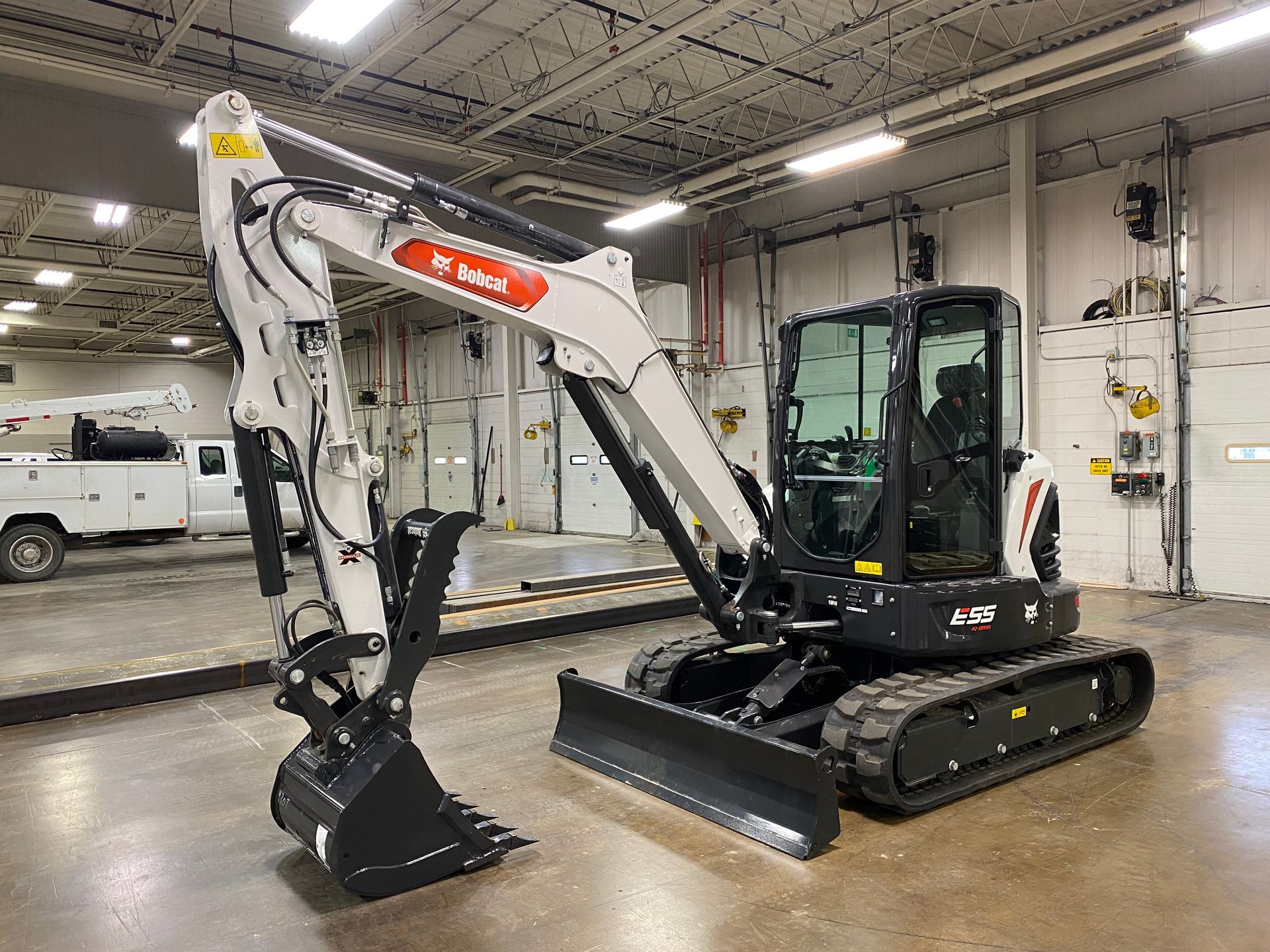 Bobcat excavator in a garage, black and white with a bucket attachment, ready for use.