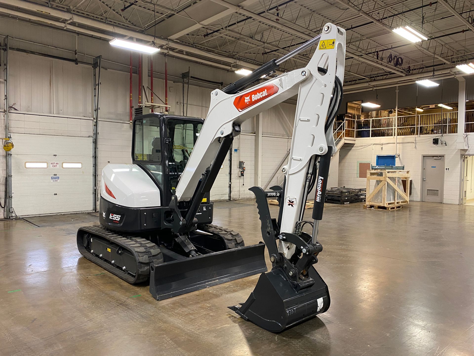 White Bobcat excavator in a warehouse, arm extended with a bucket.