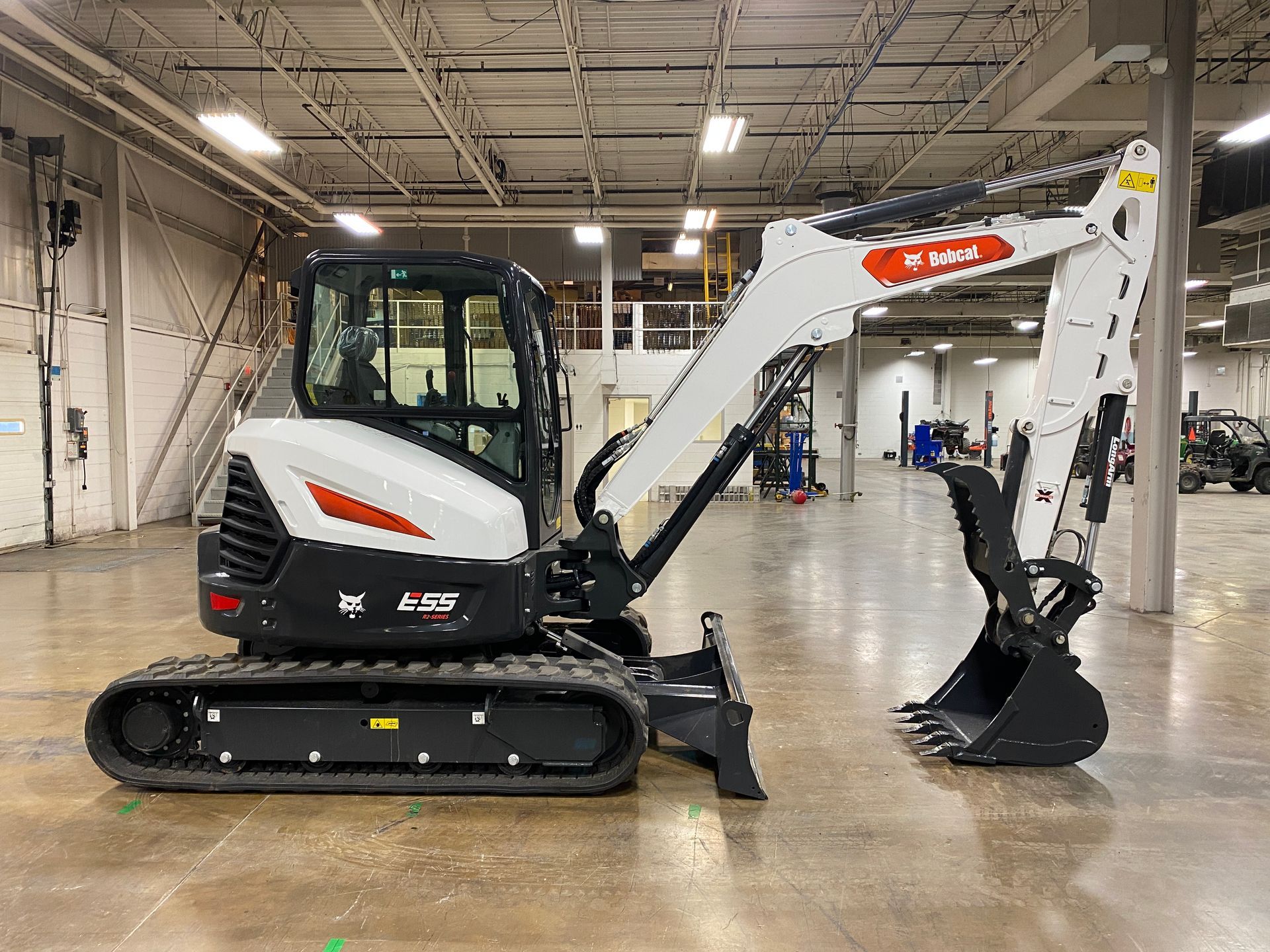 White and black Bobcat excavator with orange accents in a warehouse.