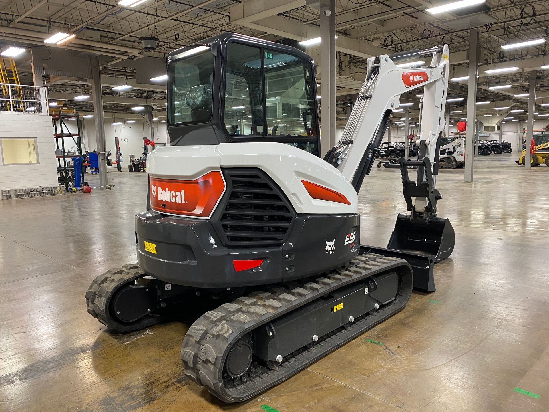 Bobcat E42 mini excavator, white and black, indoors, bucket lowered, tracks visible.