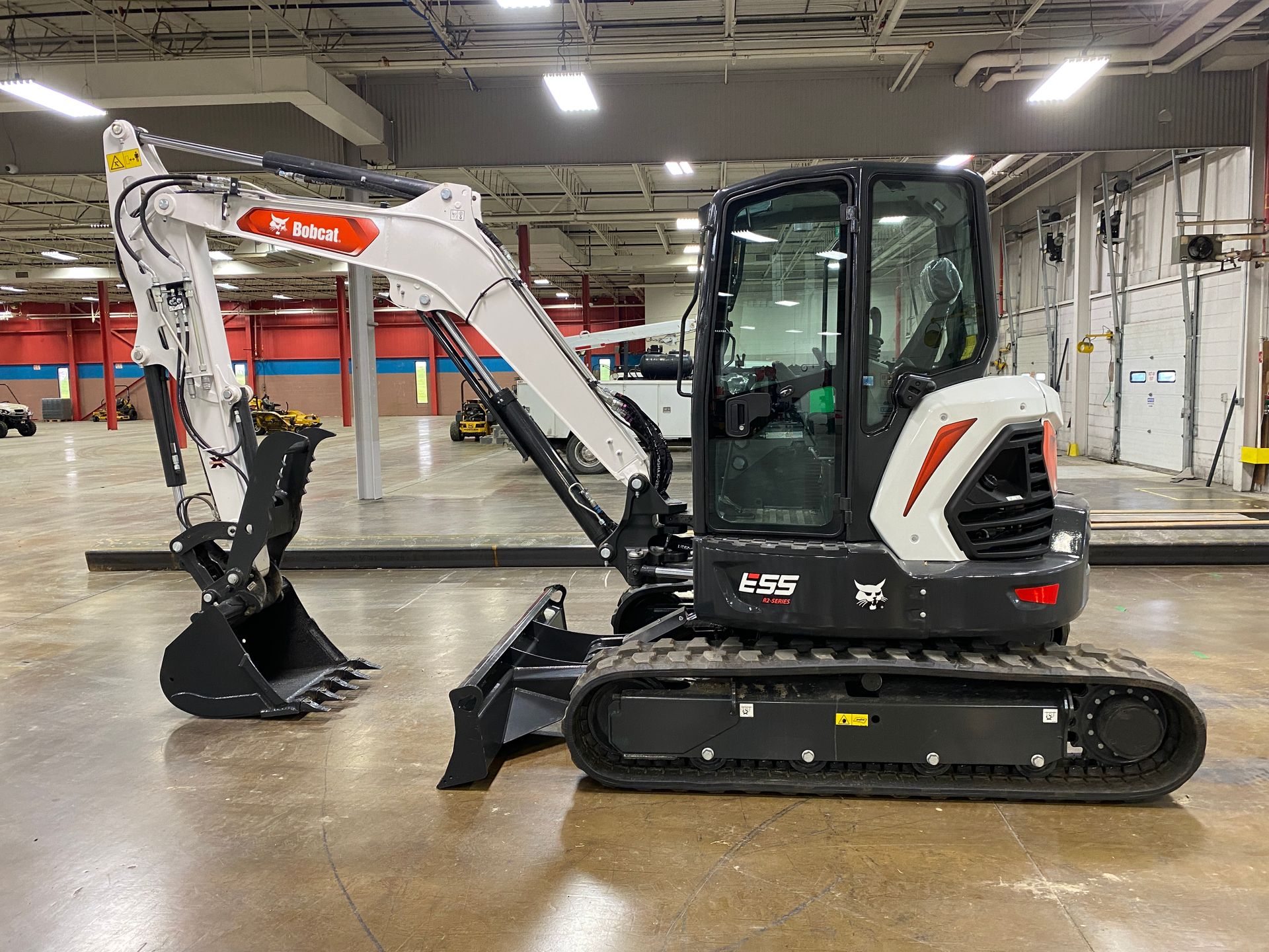 White and black Bobcat excavator with arm extended, parked indoors.