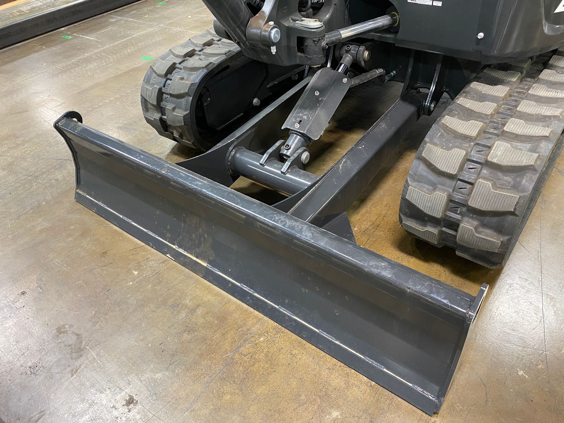 Mini excavator with a front blade on a concrete floor.