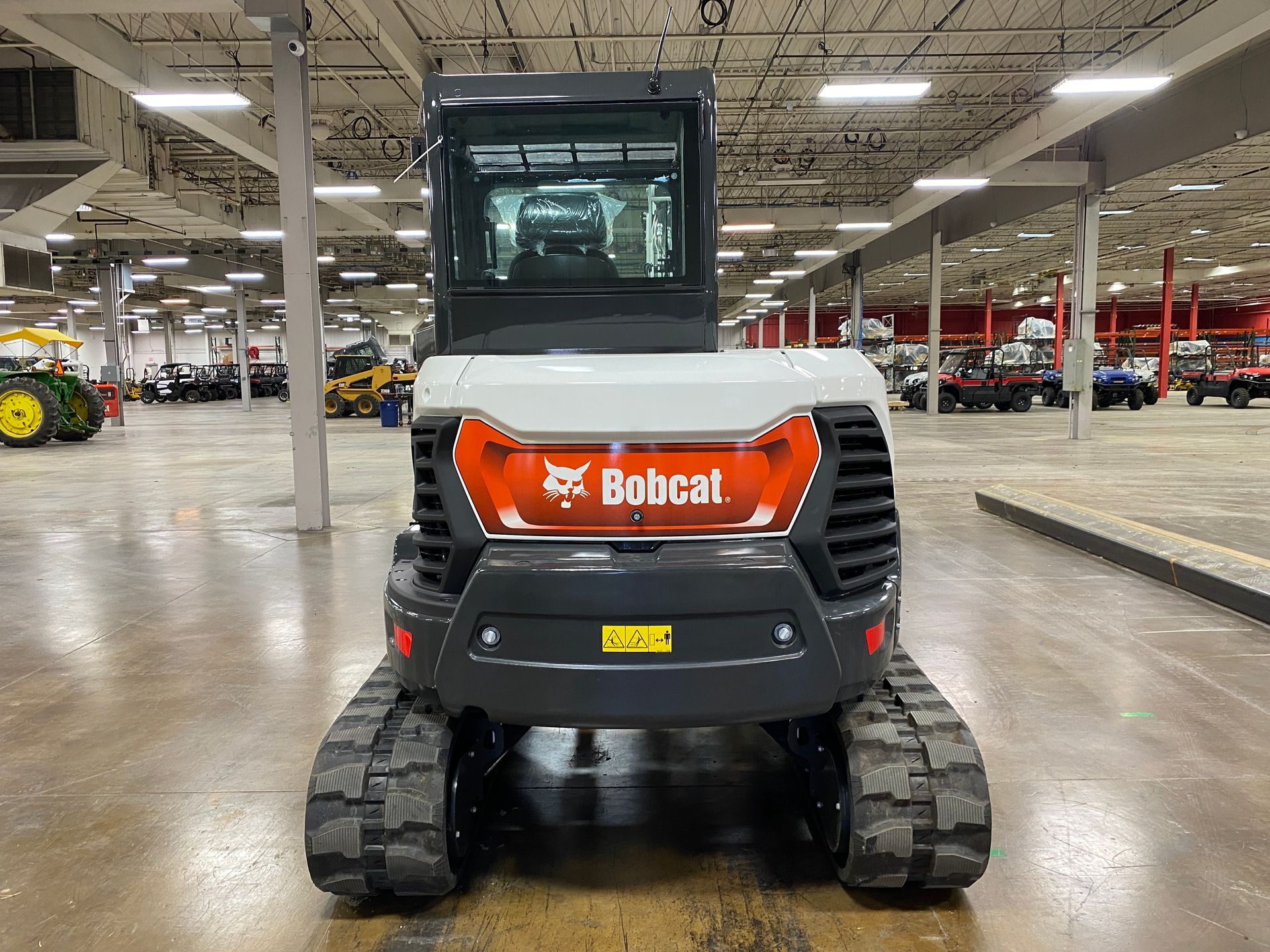Gray and white Bobcat excavator with orange logo, black tracks, in a warehouse setting.