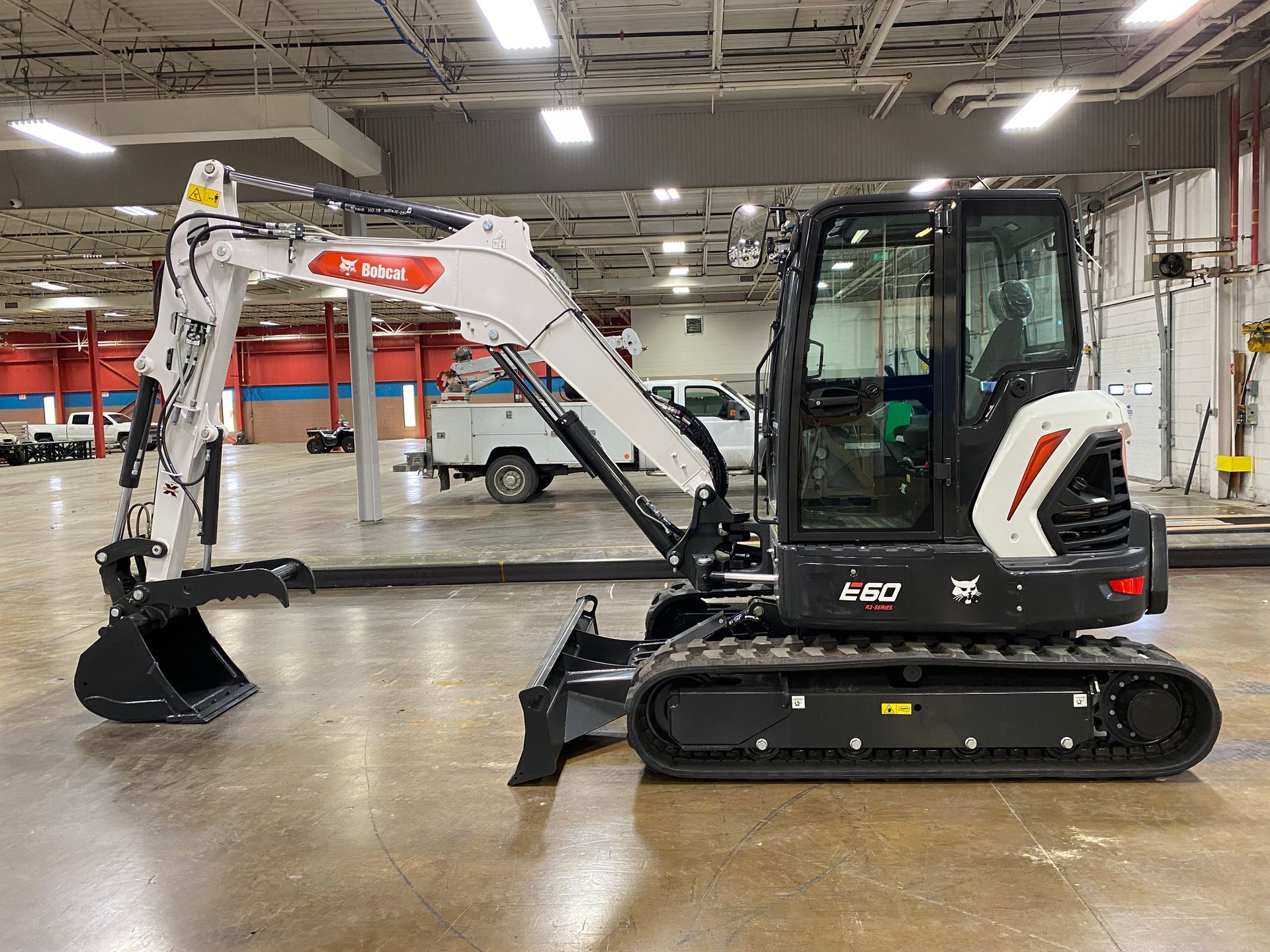 Bobcat E32 compact excavator on display inside a building. White and black machine, front bucket extended.