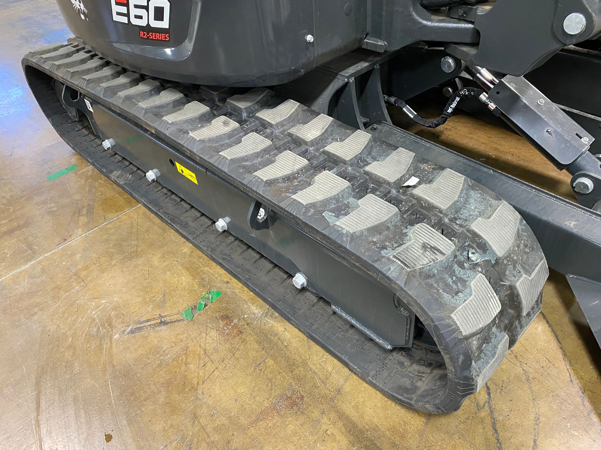 Close-up of a dark grey Bobcat E60 excavator track on a wooden floor.
