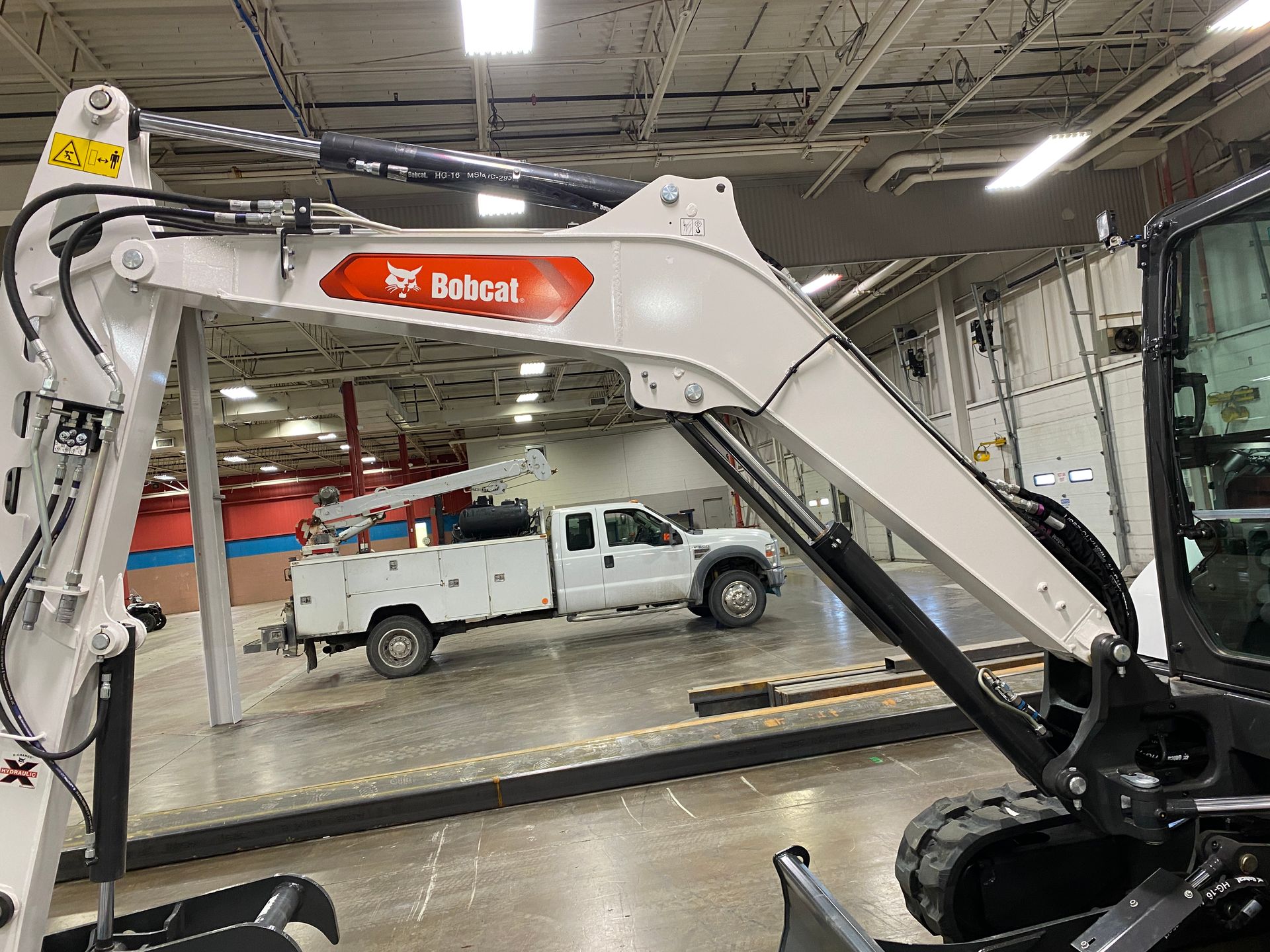 White Bobcat excavator arm with orange logo, indoors near a white pickup truck.