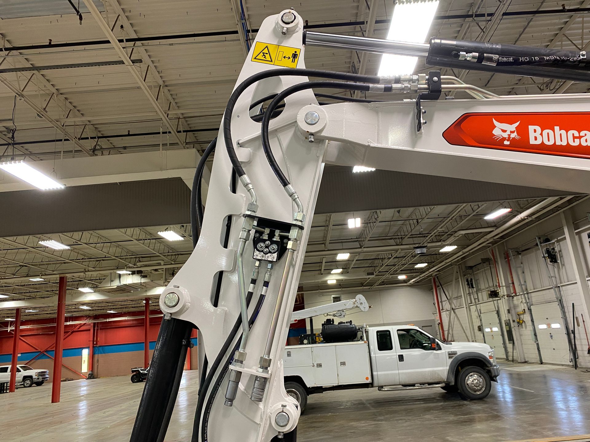 White Bobcat excavator arm with hydraulic lines, inside a shop with a white truck.