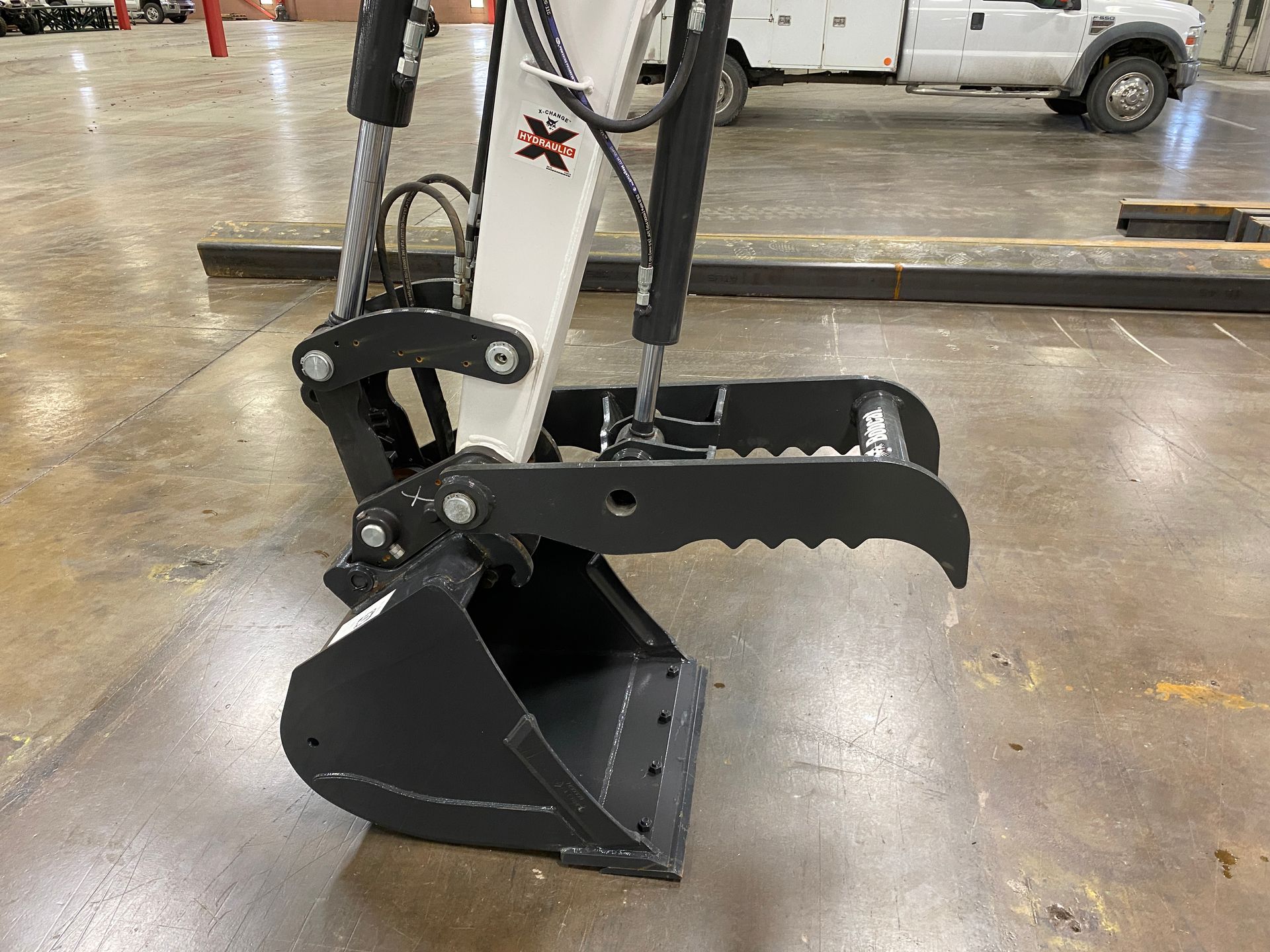 Bobcat excavator bucket with a grapple attachment, black and white, indoors.
