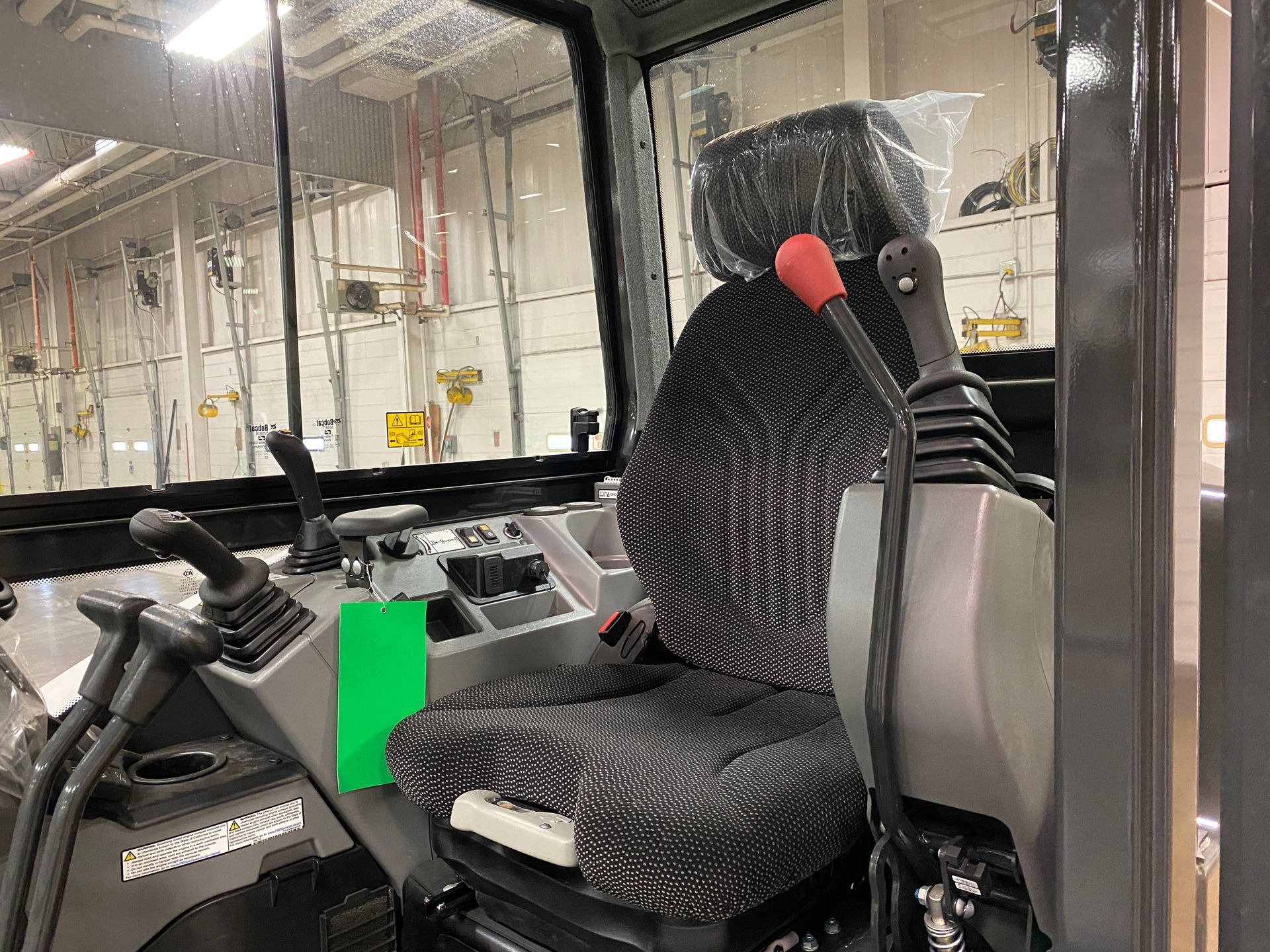 Interior cab of a construction vehicle with a seat, controls, and windshield.