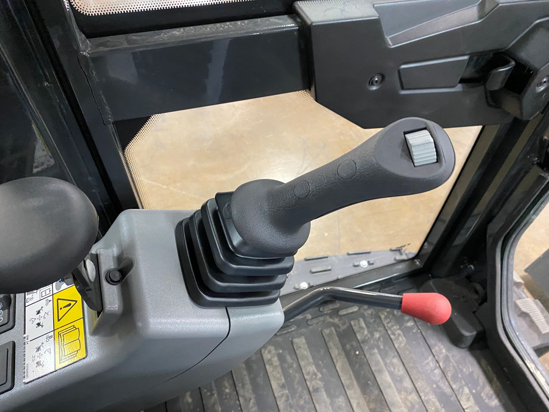 Black excavator joystick with a gray base and a red lever. Inside the cab.