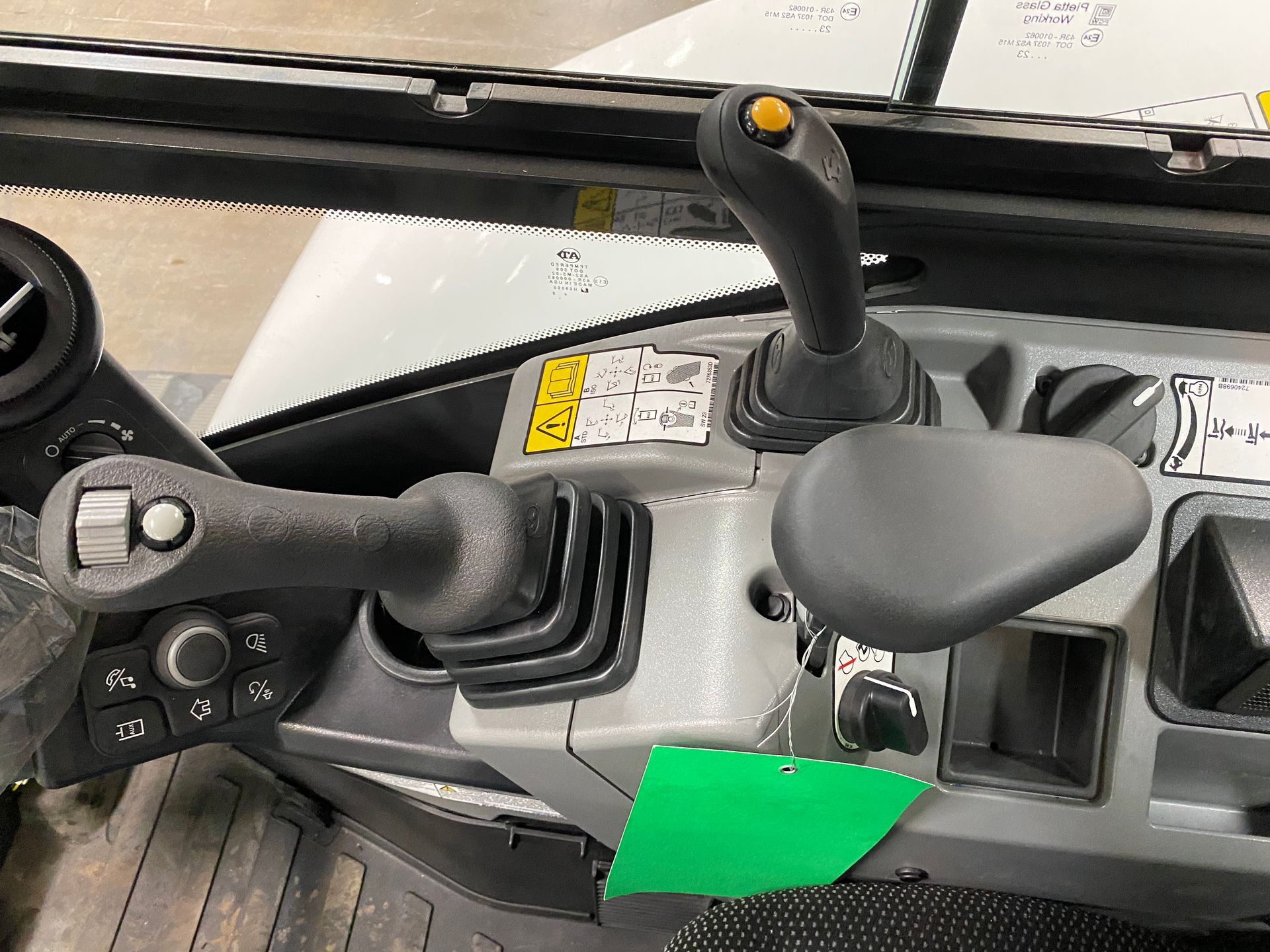 Close-up of excavator controls: two joysticks, a yellow knob, and a black lever on a gray panel.