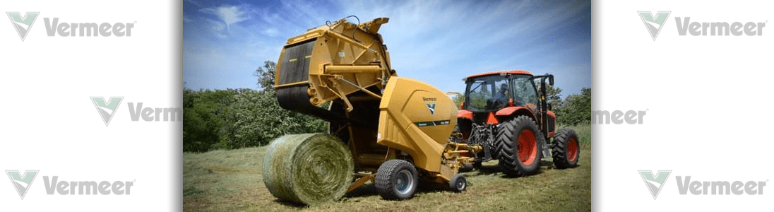 A tractor pulling a yellow hay baler in a field, creating a large round bale.